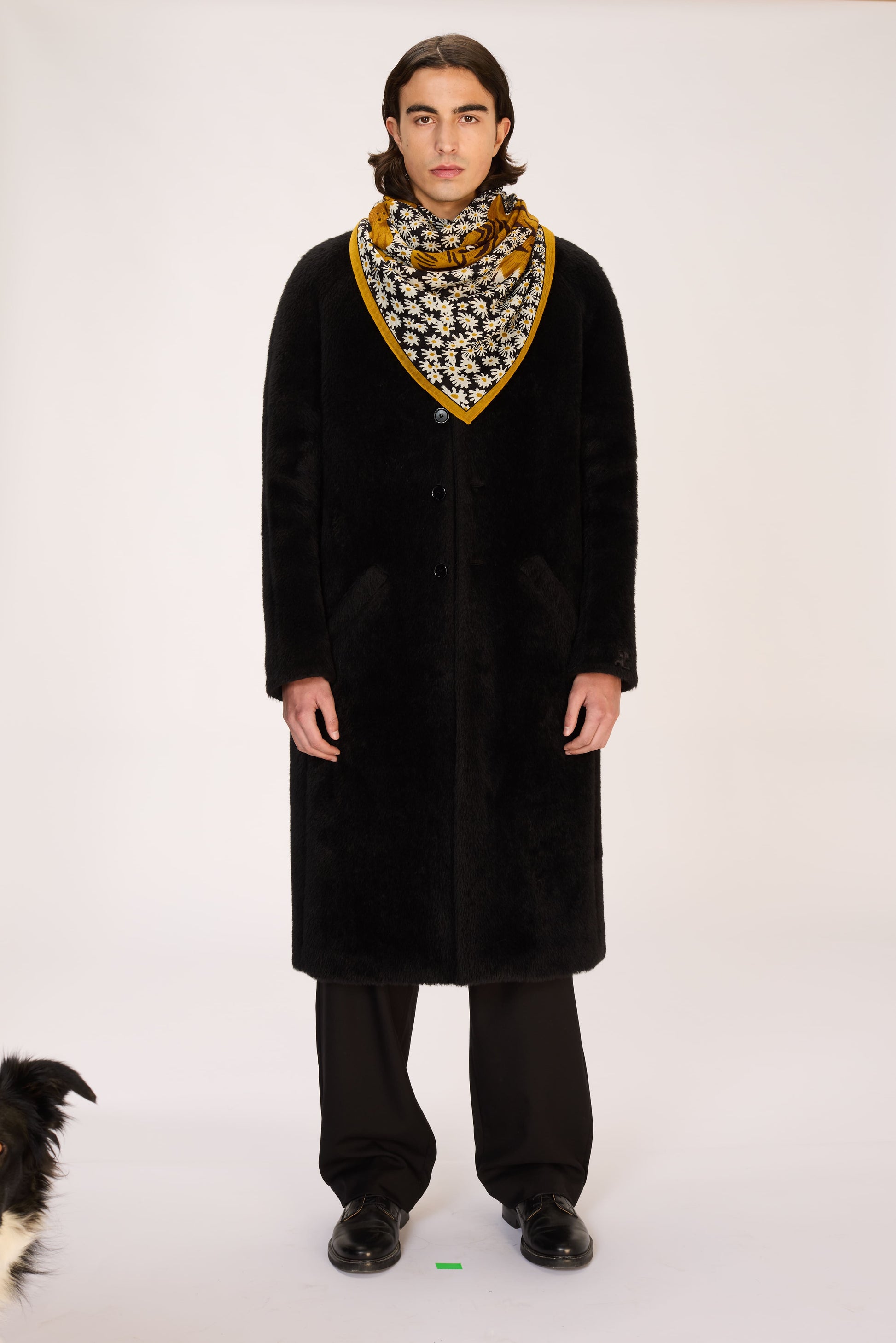 Person wearing a long black coat and patterned scarf on a white background