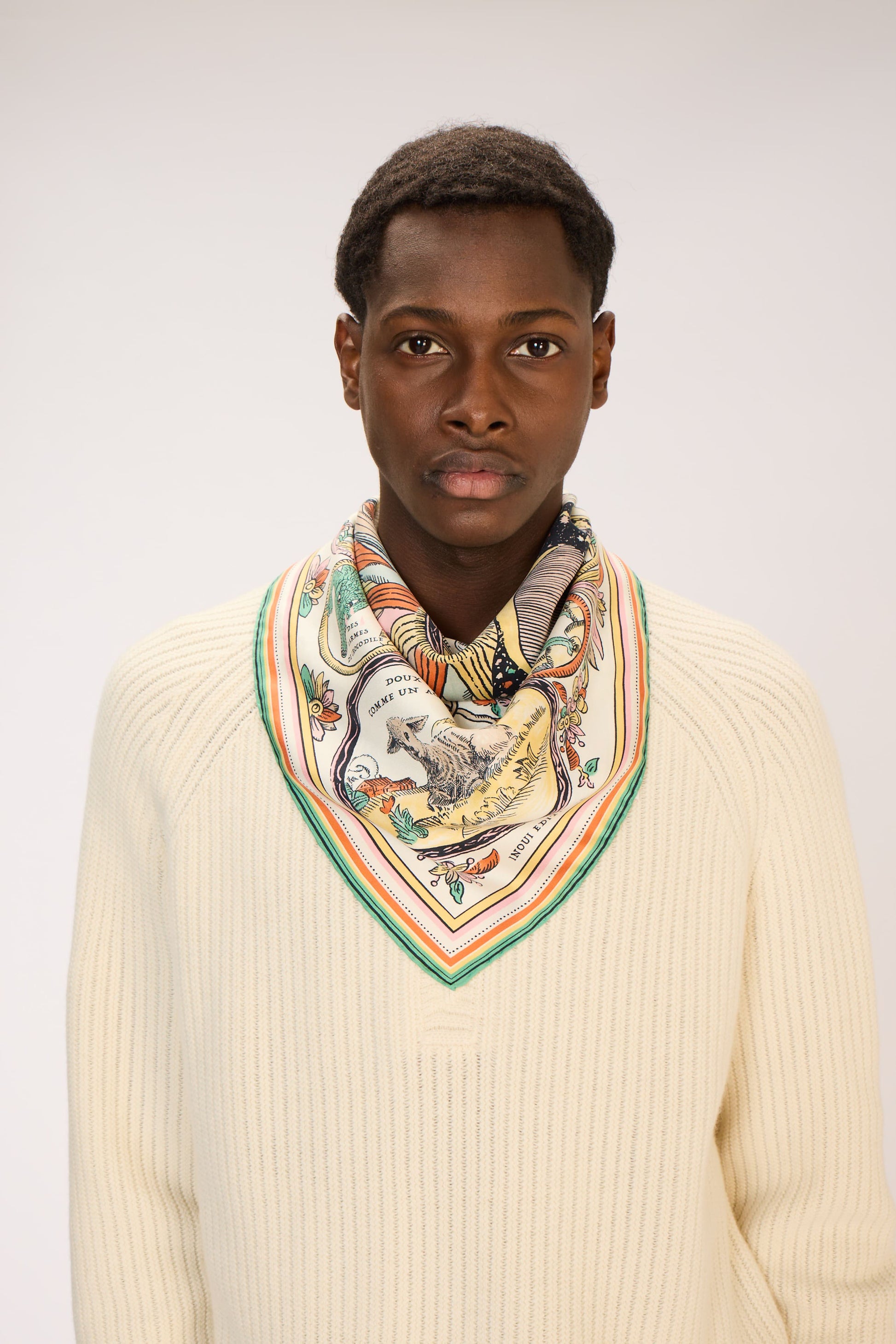 Person wearing a patterned scarf and cream sweater against a plain background