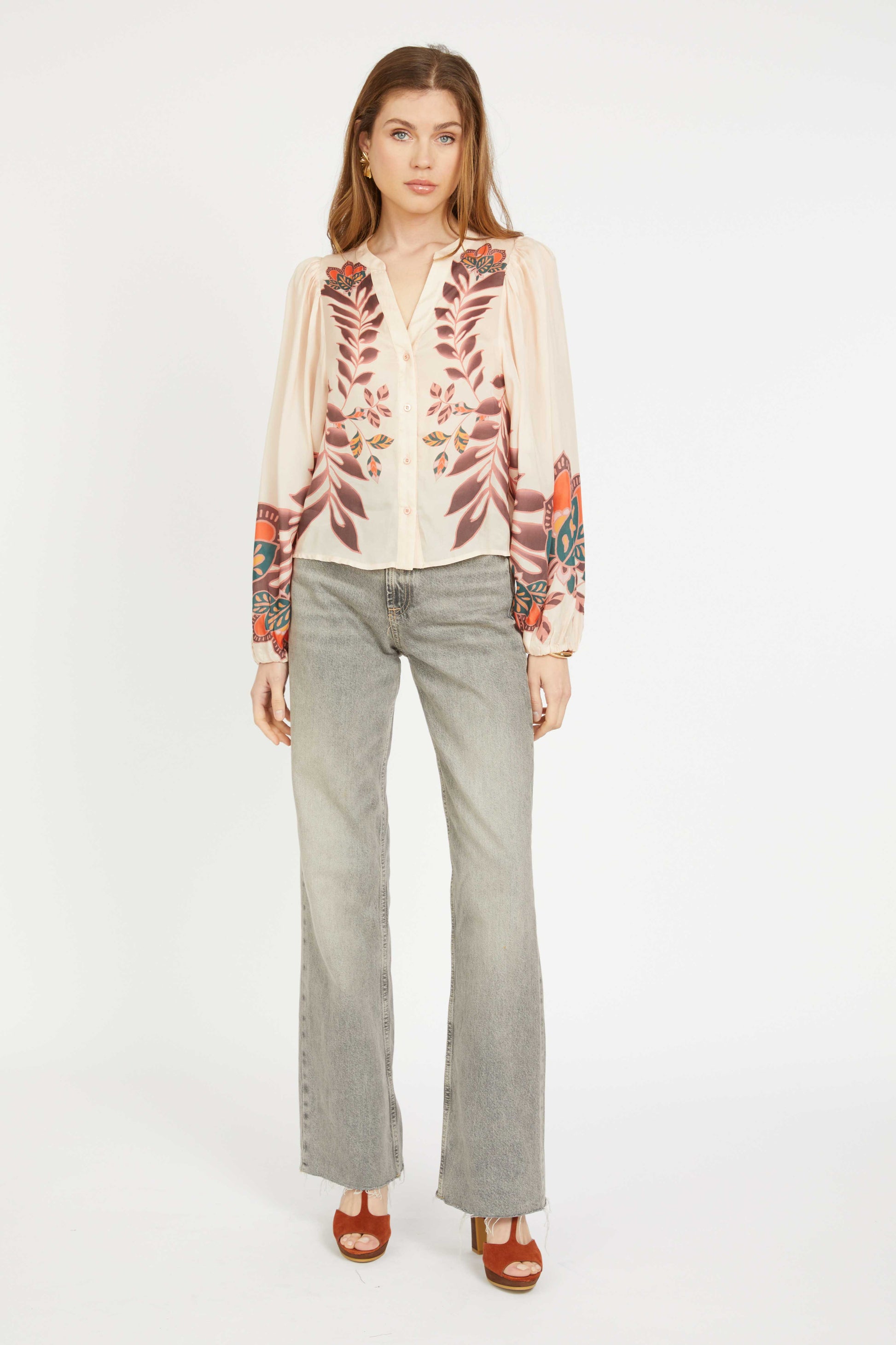 Woman wearing a patterned blouse and gray pants on a white background