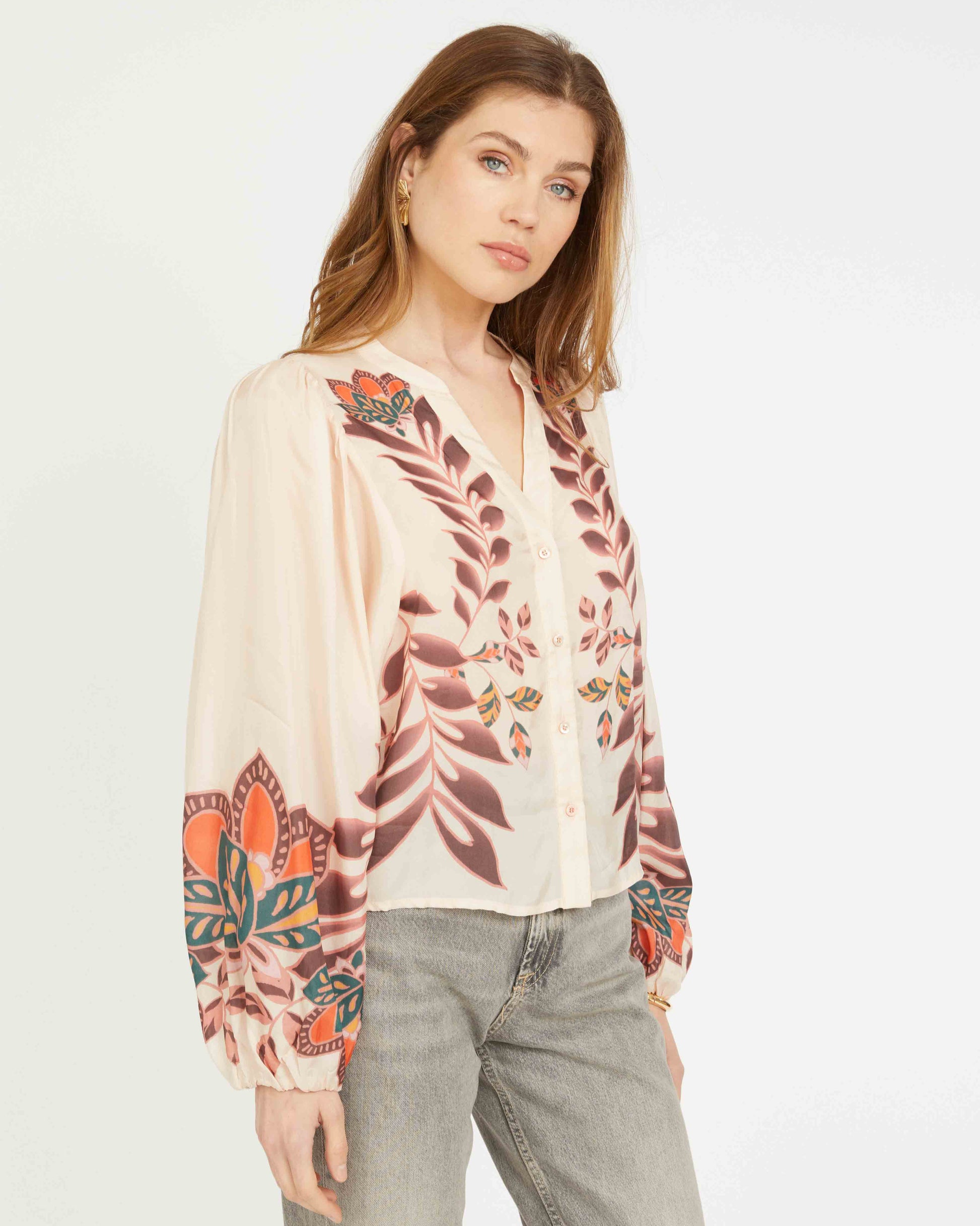 Woman wearing a floral blouse with long sleeves and gray pants on a white background