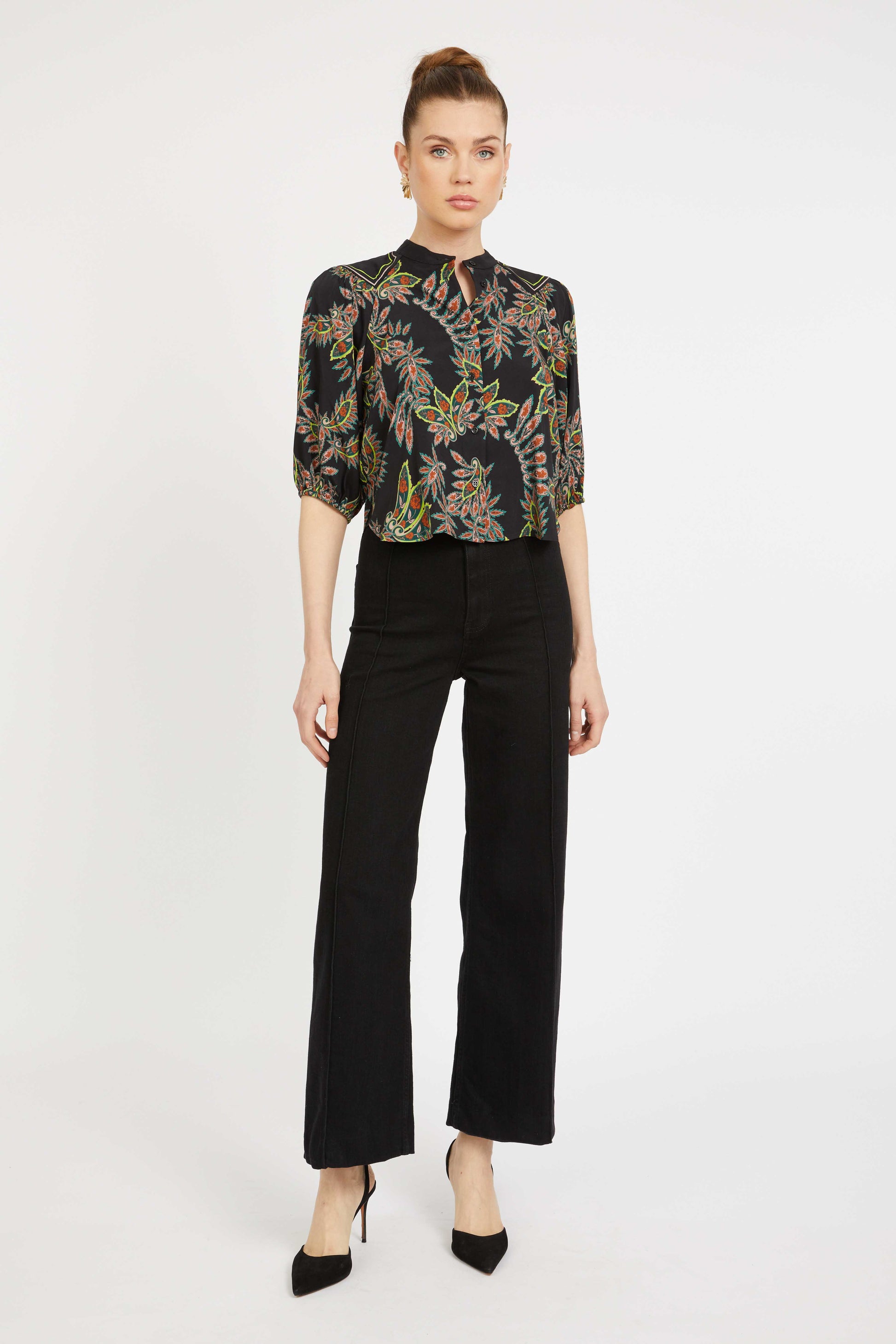 Woman wearing a black floral blouse and black pants on a white background