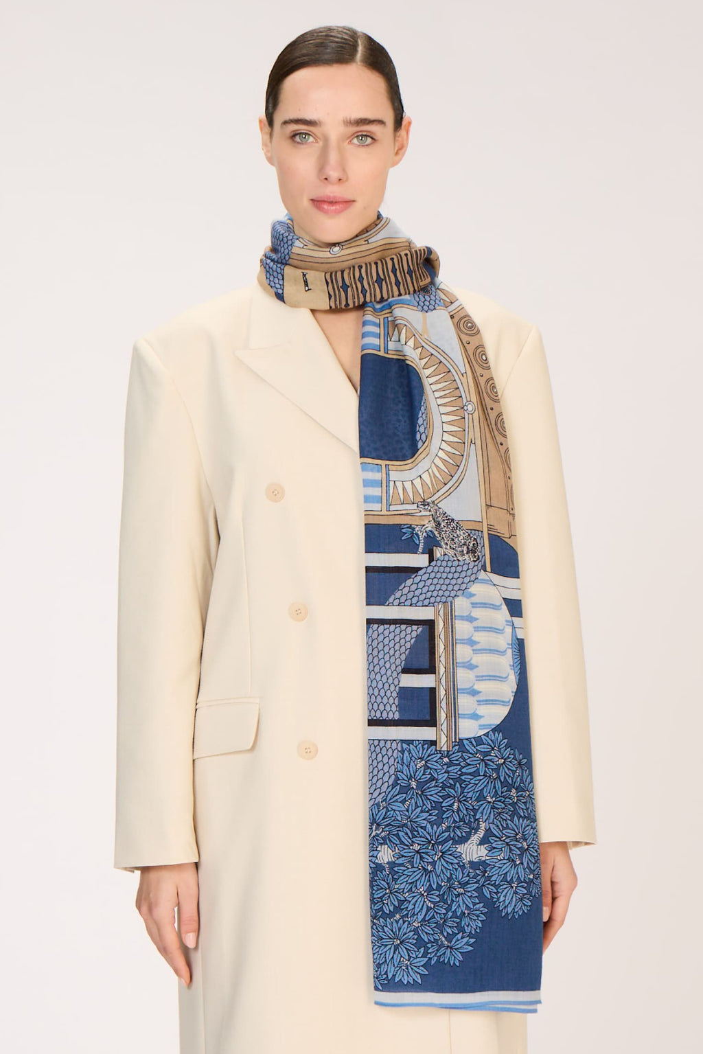 Person wearing a long cream coat with a patterned scarf on a white background
