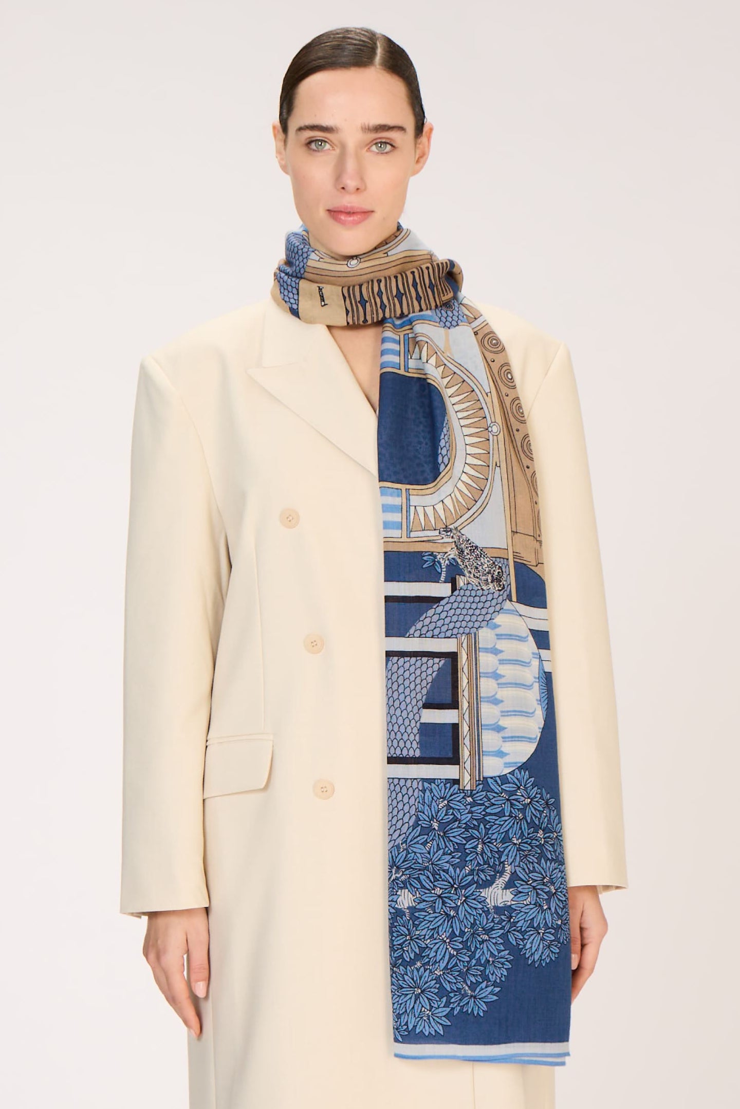 Person wearing a long cream coat with a patterned scarf on a white background