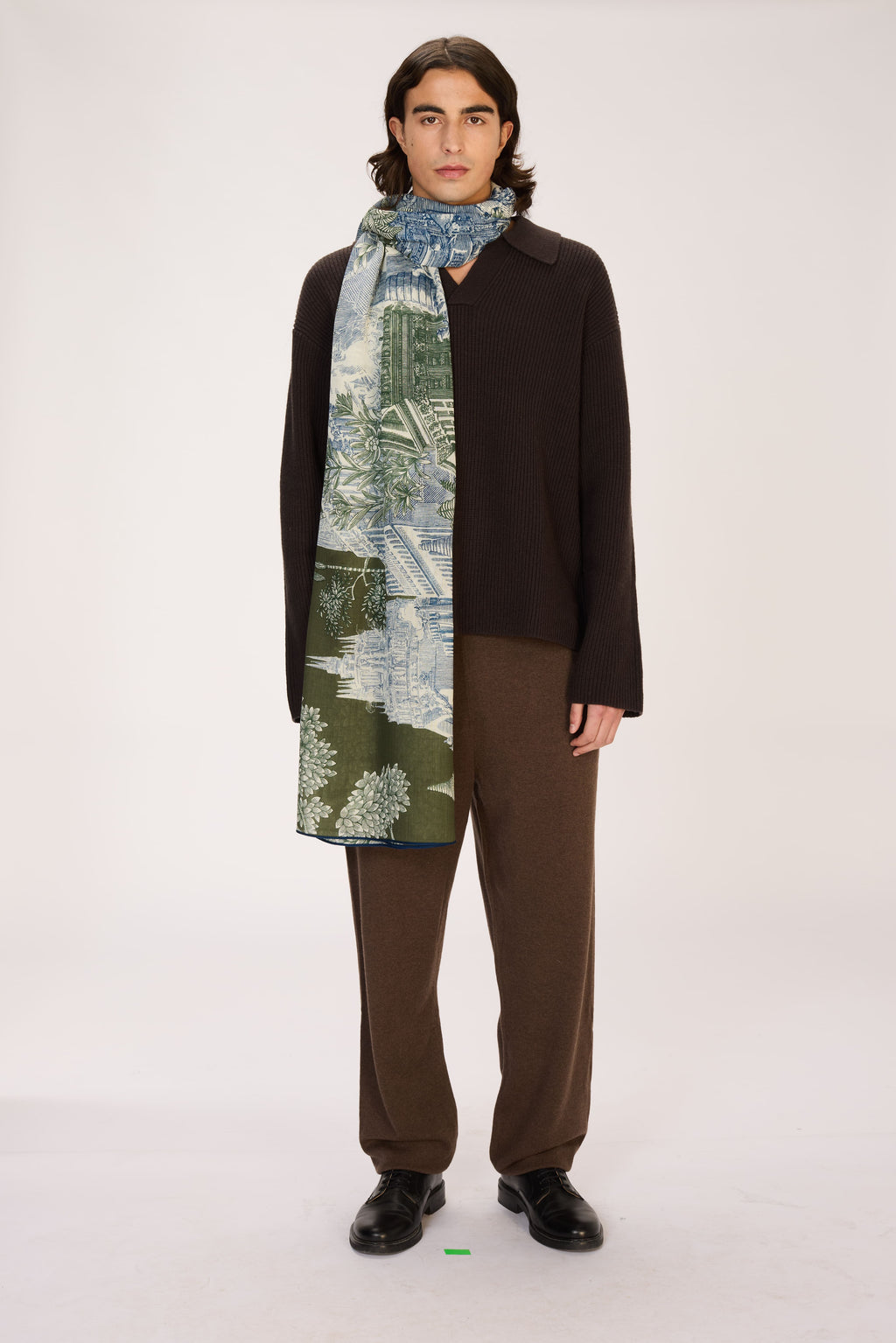 Person wearing a long, patterned scarf with a neutral background