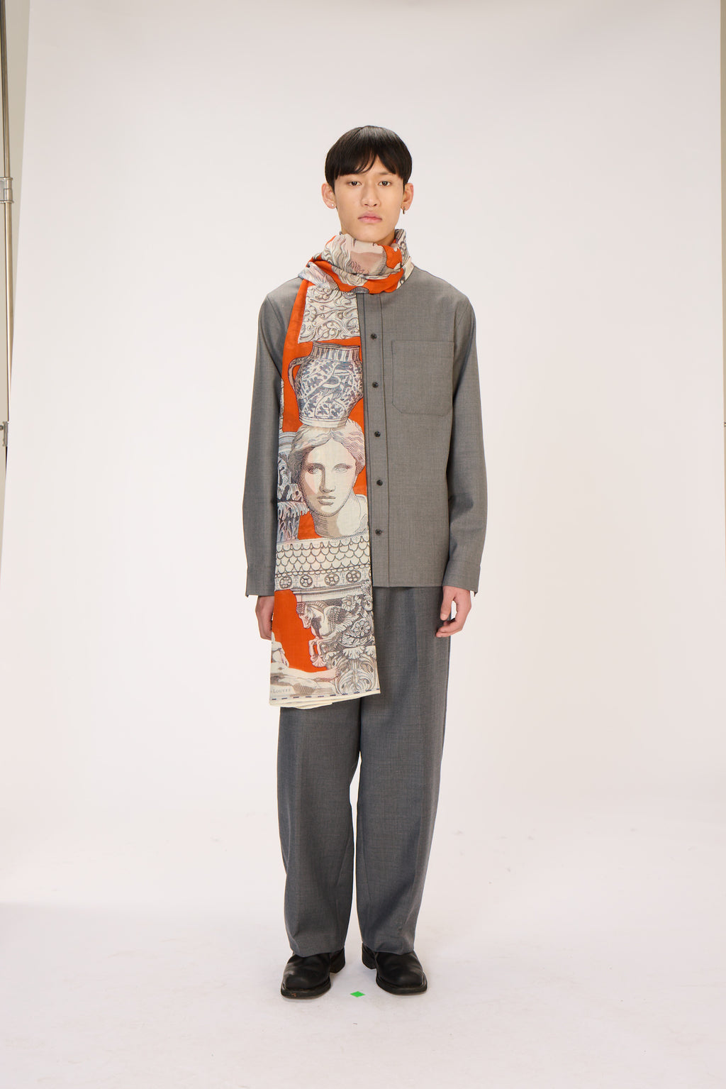 Person wearing a gray outfit with a patterned scarf on a white background