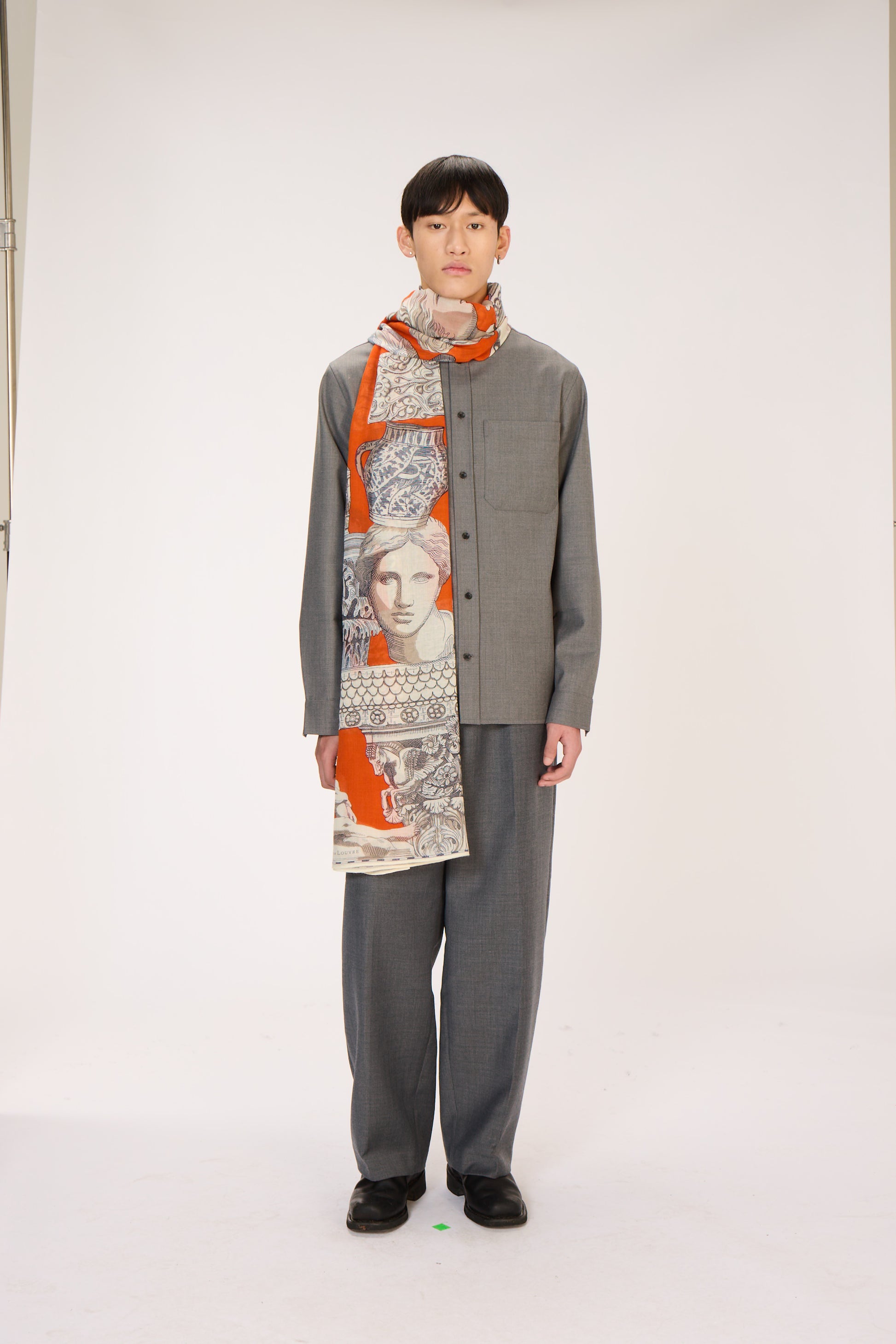 Person wearing a gray outfit with a patterned scarf on a white background