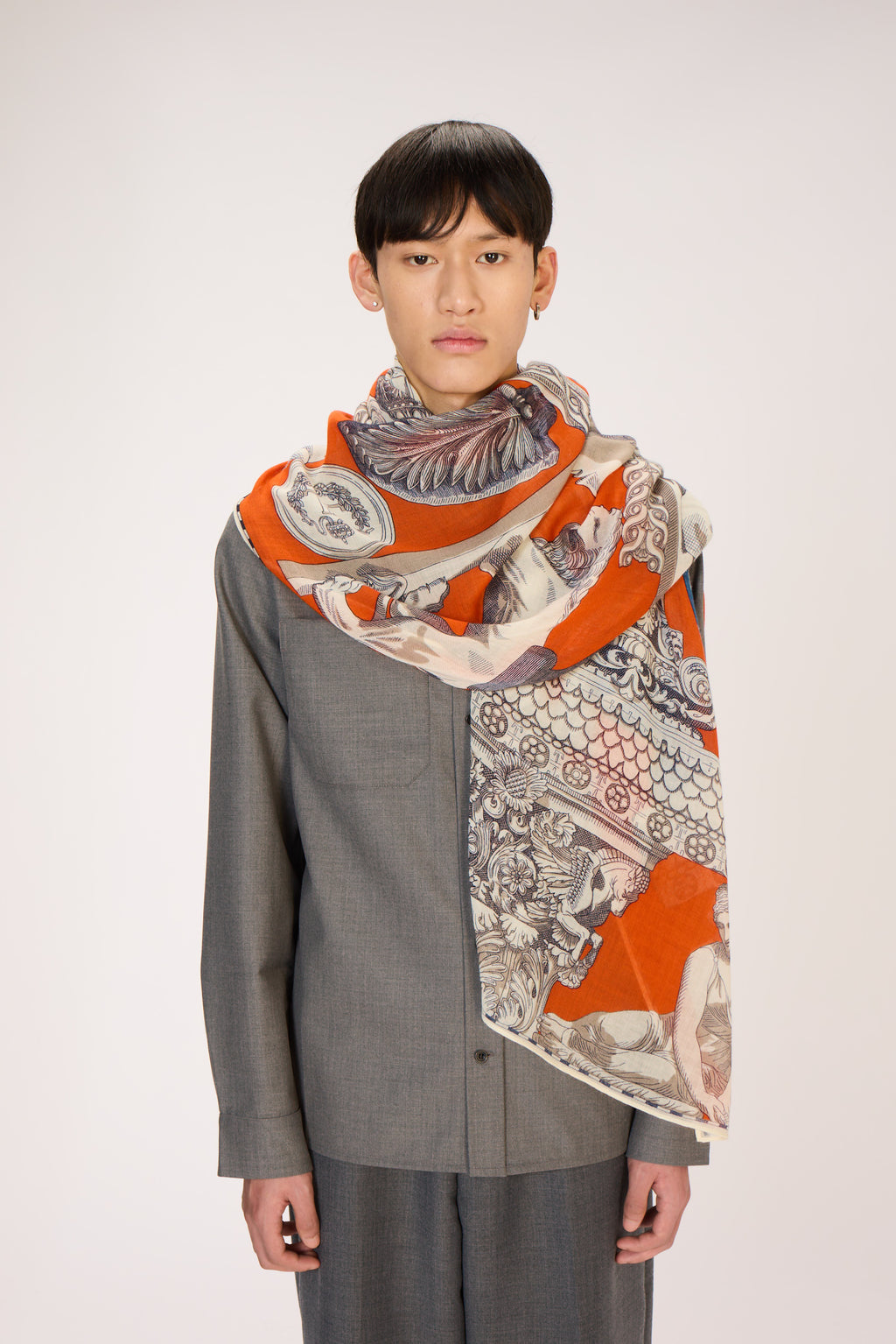 Person wearing a patterned scarf with orange and gray design on a plain background