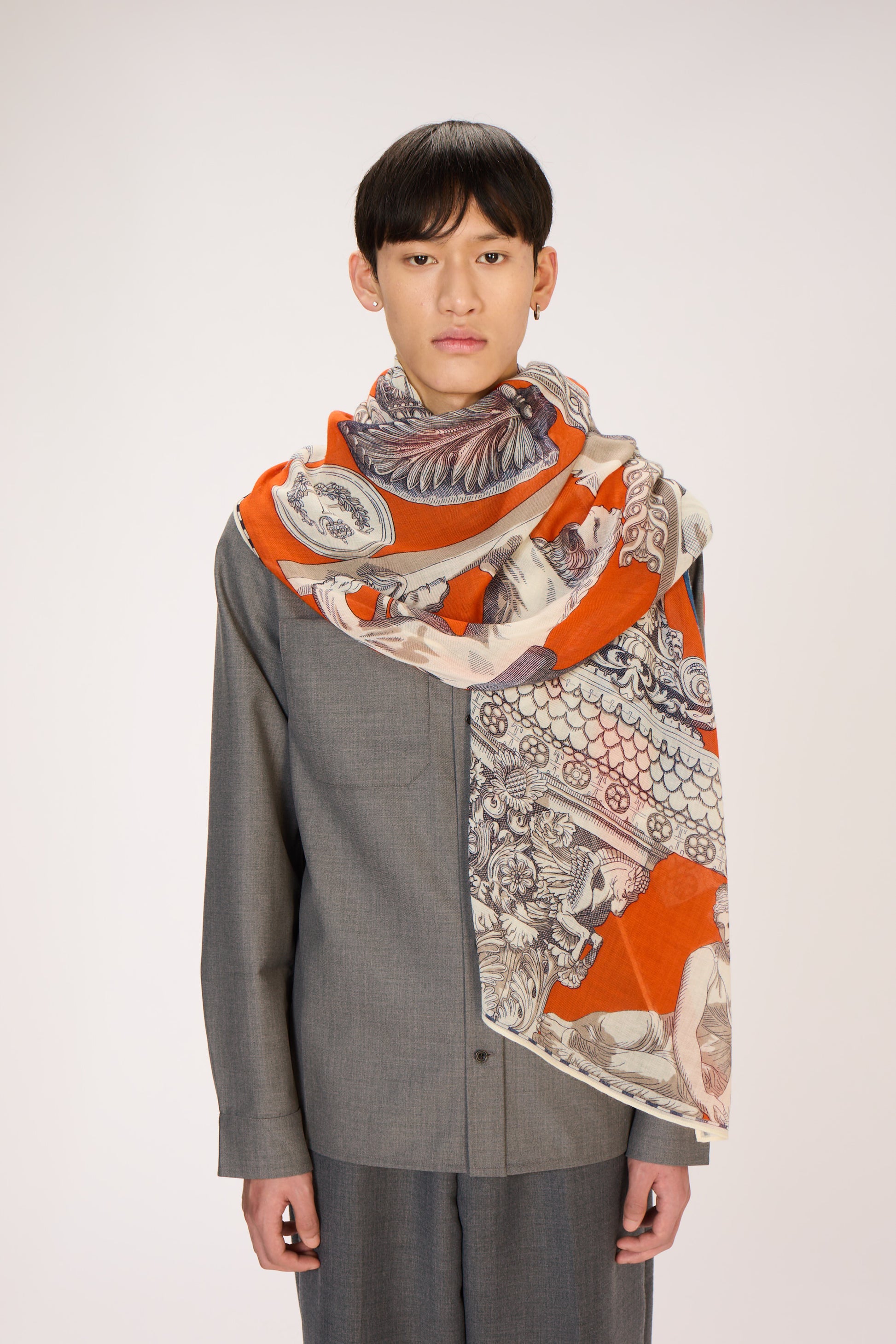 Person wearing a patterned scarf with orange and gray design on a plain background