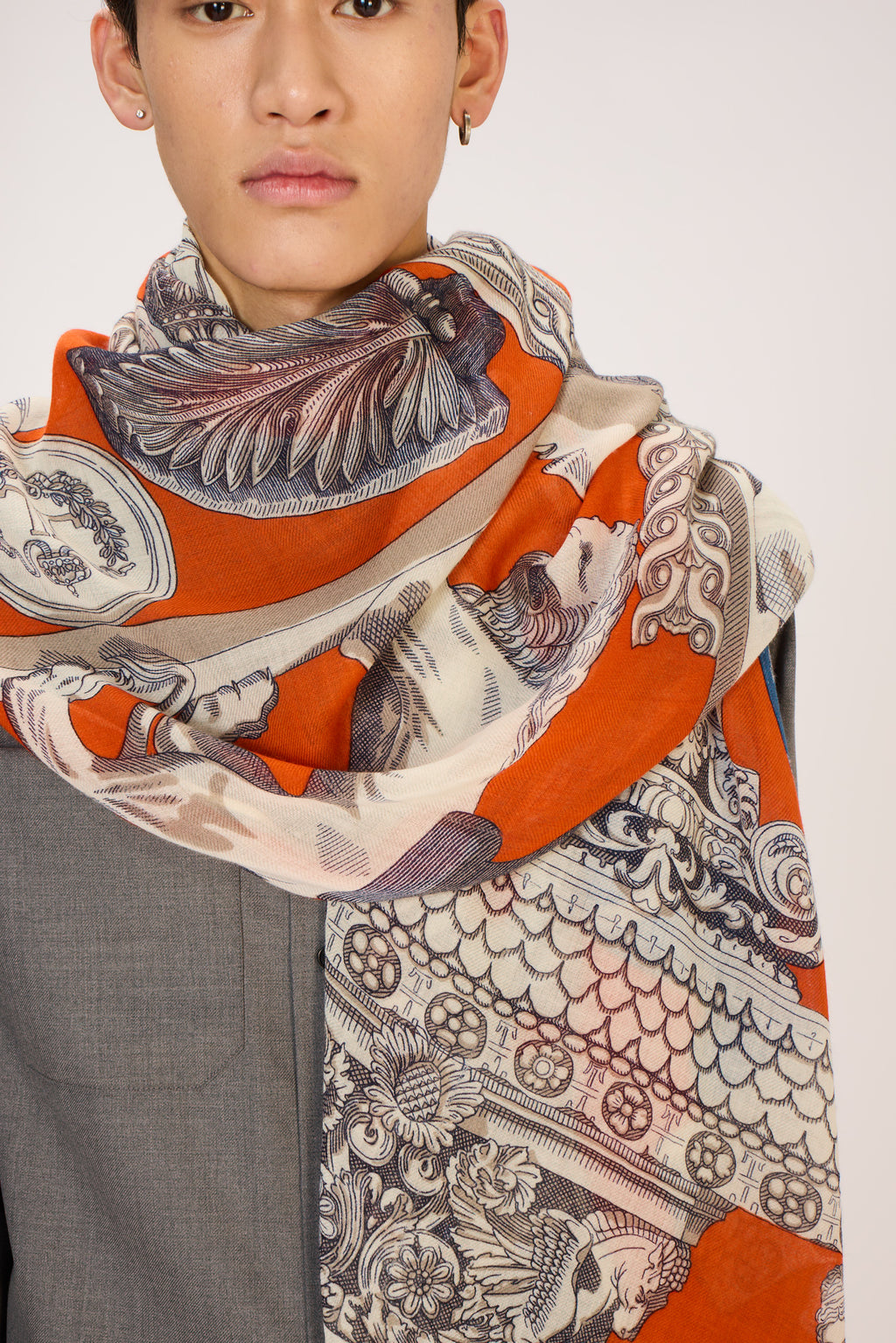 Person wearing a patterned scarf with orange, beige, and black design on a plain background