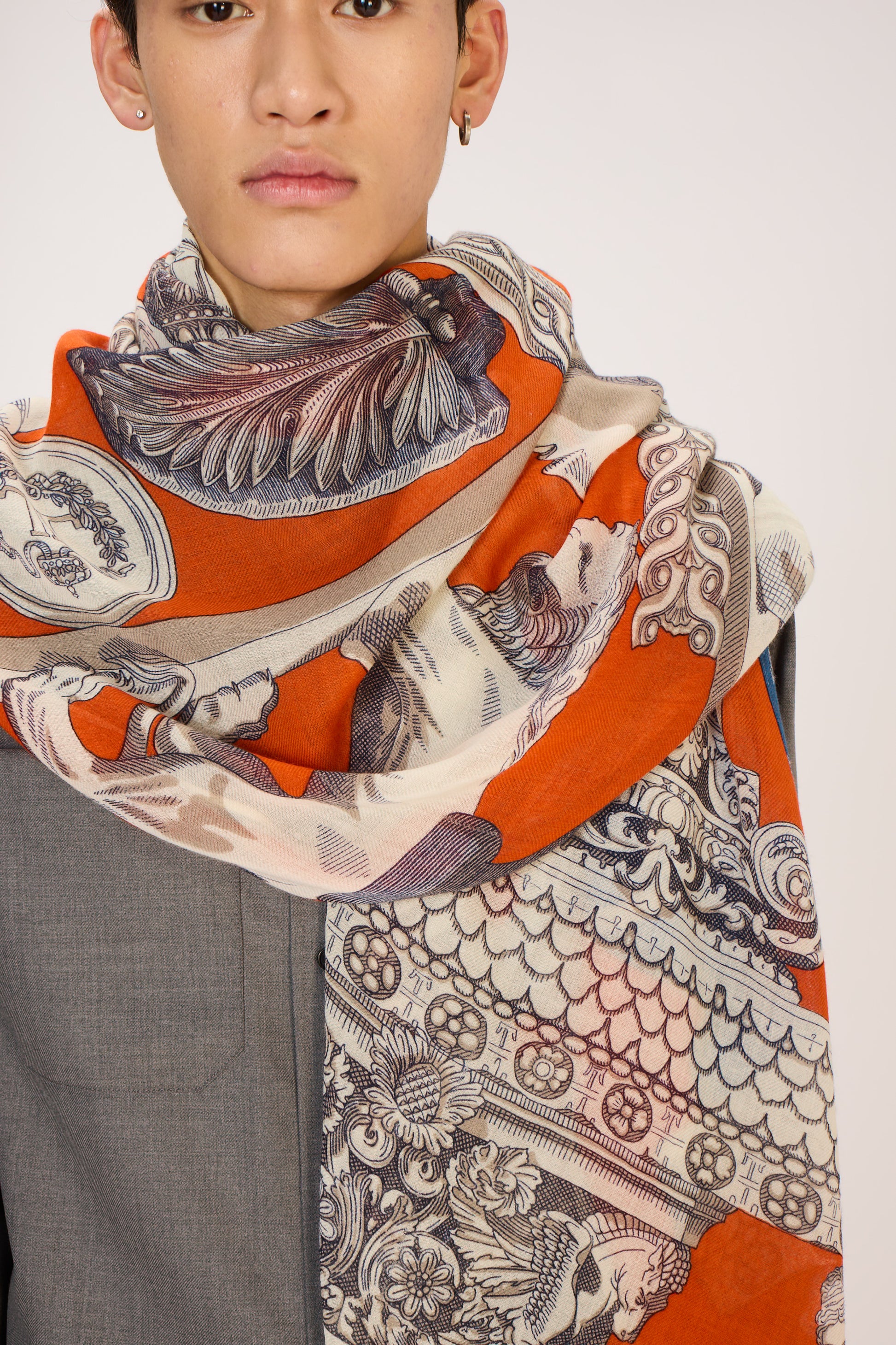 Person wearing a patterned scarf with orange, beige, and black design on a plain background