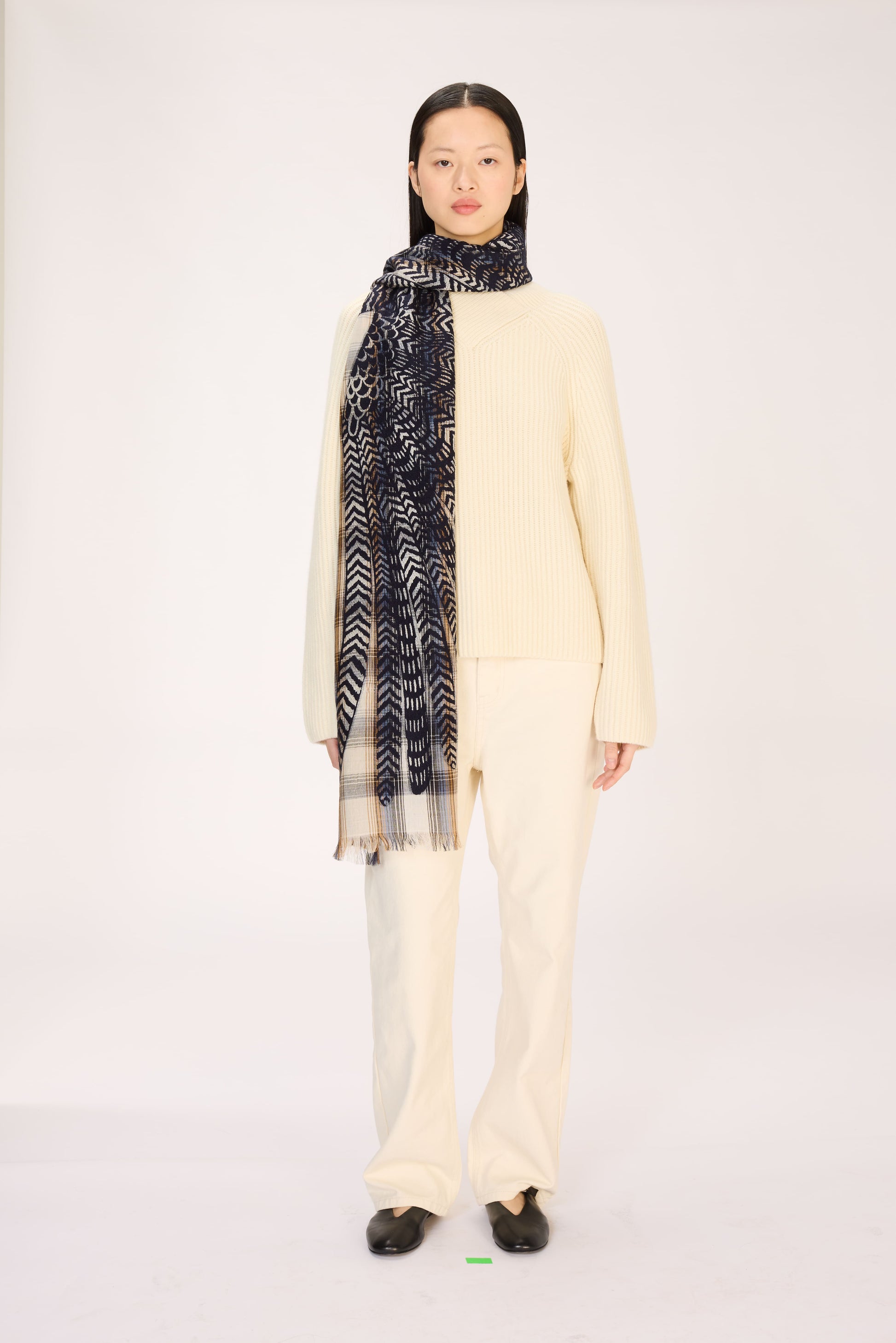 Person wearing a cream sweater and patterned scarf on a white background