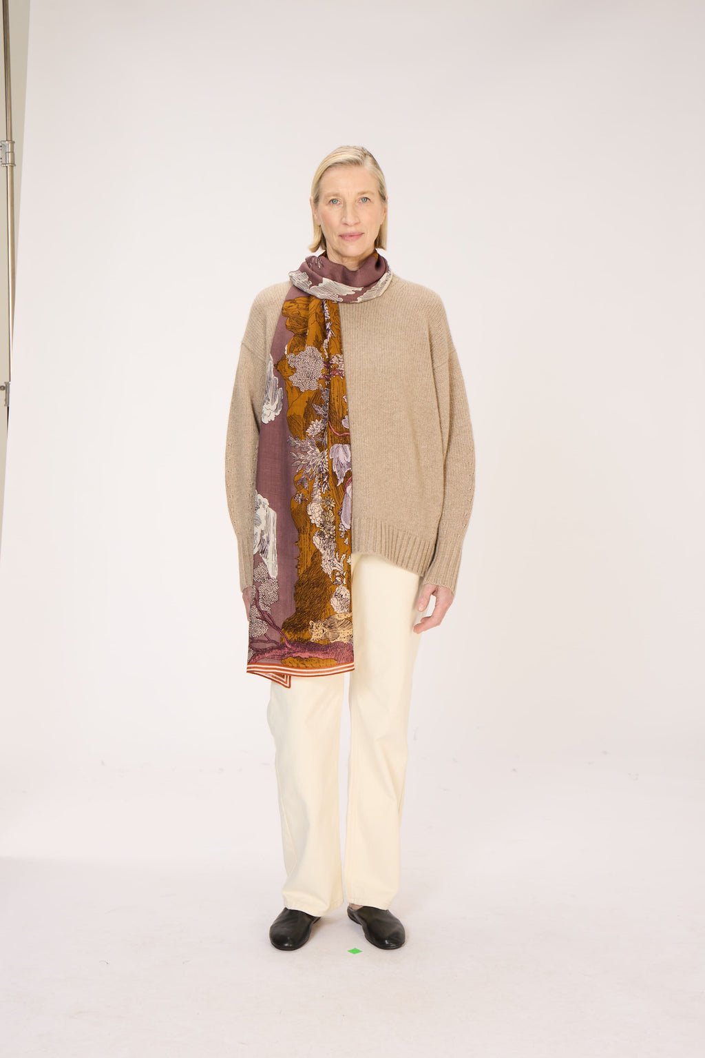 Person wearing a beige sweater and floral scarf on a white background