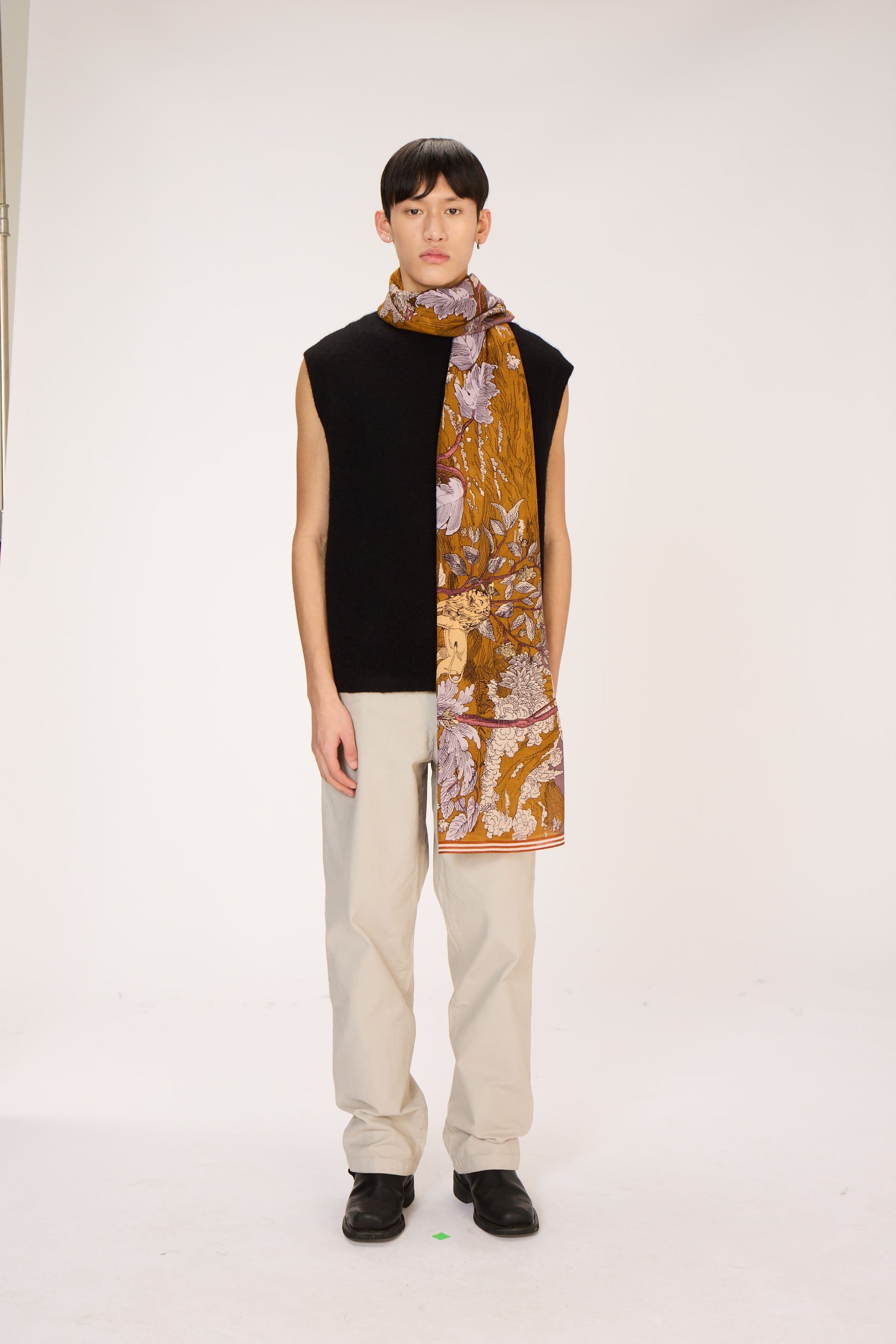 Person wearing a floral scarf with a black top and beige pants on a white background