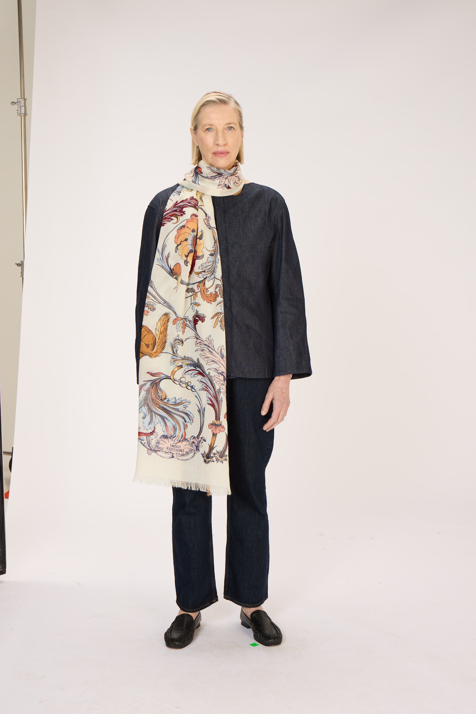 Woman wearing a patterned scarf and dark outfit on a white background