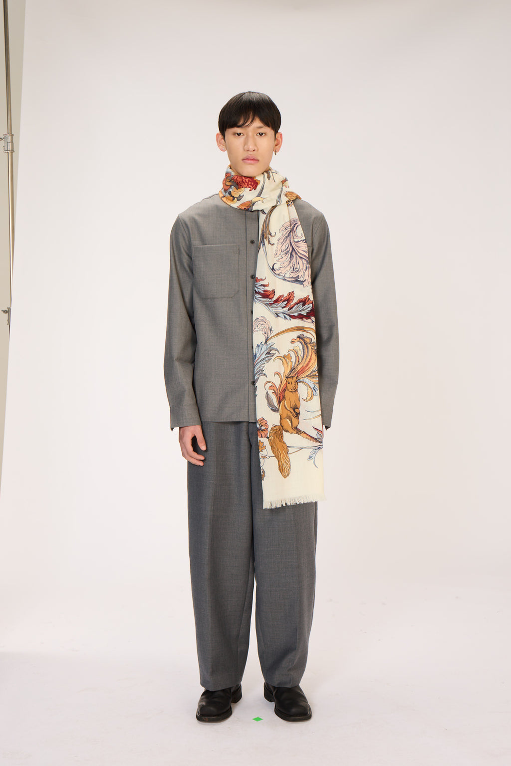 Person wearing a gray outfit with a patterned scarf on a white background