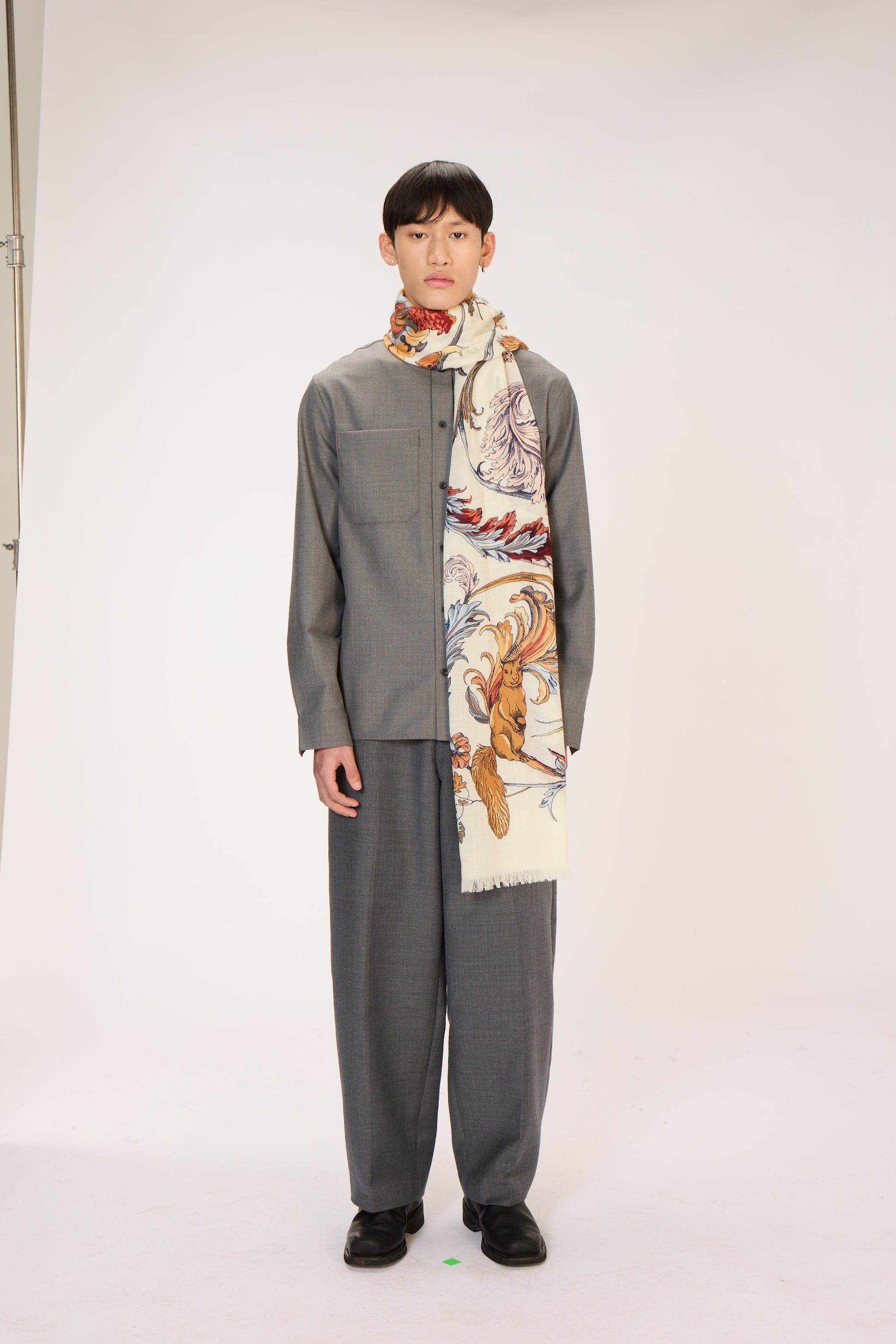 Person wearing a gray outfit with a patterned scarf on a white background