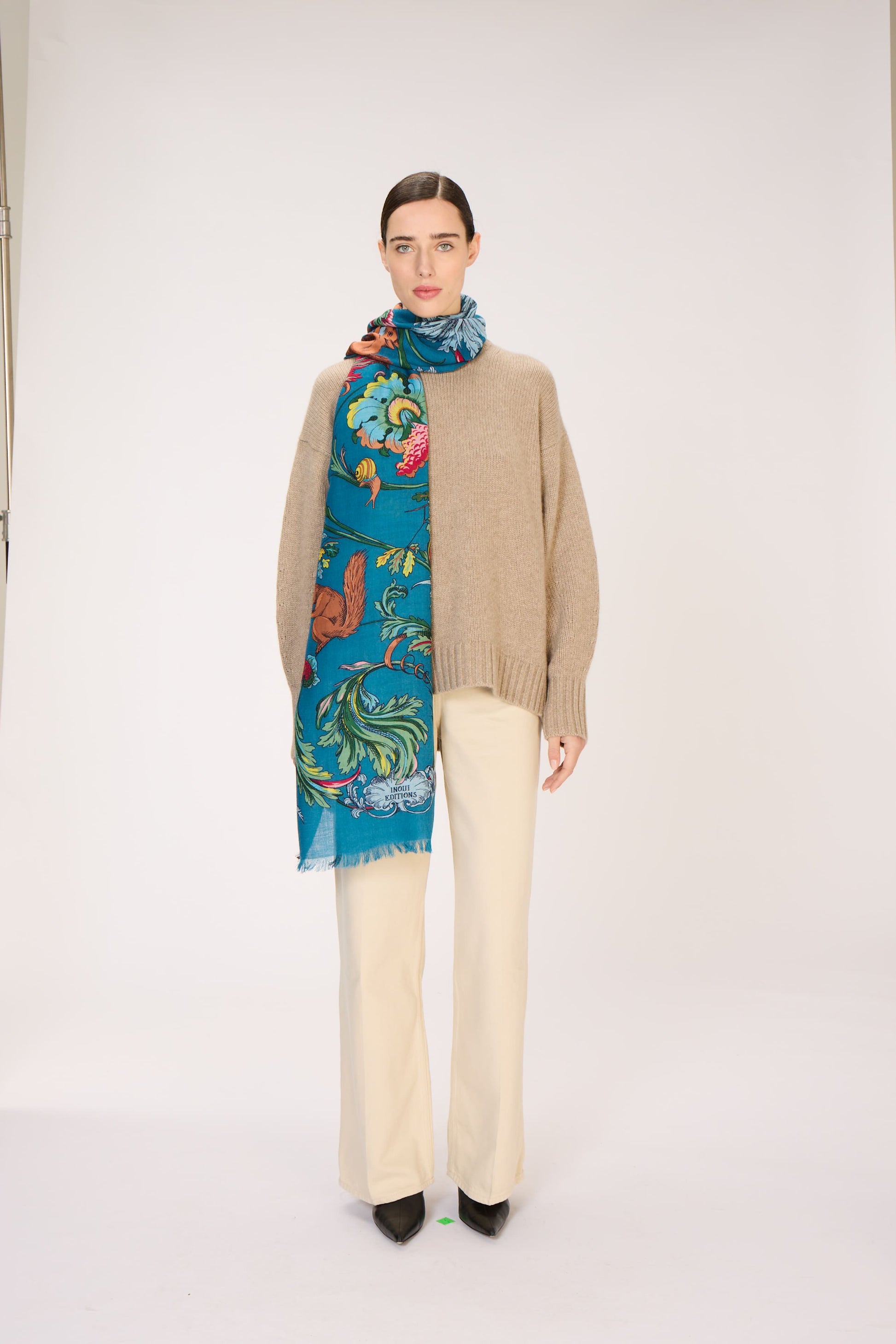 Woman wearing a beige sweater and colorful scarf on a white background