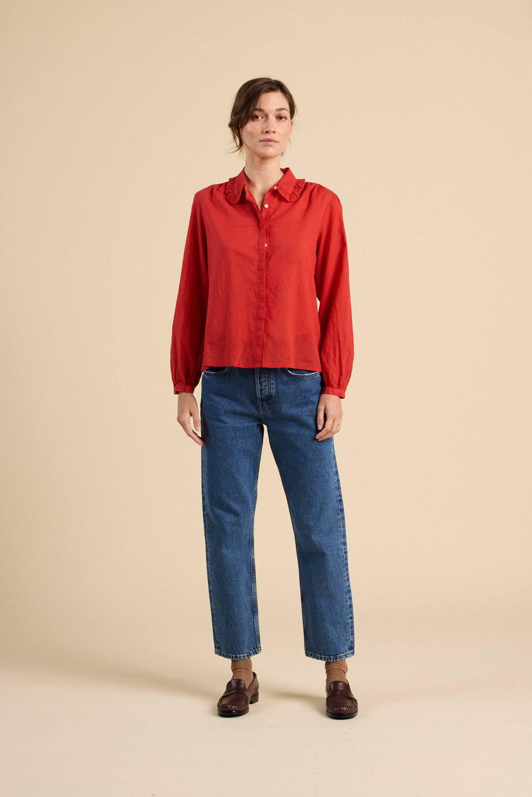 Person wearing a red shirt and blue jeans on a beige background