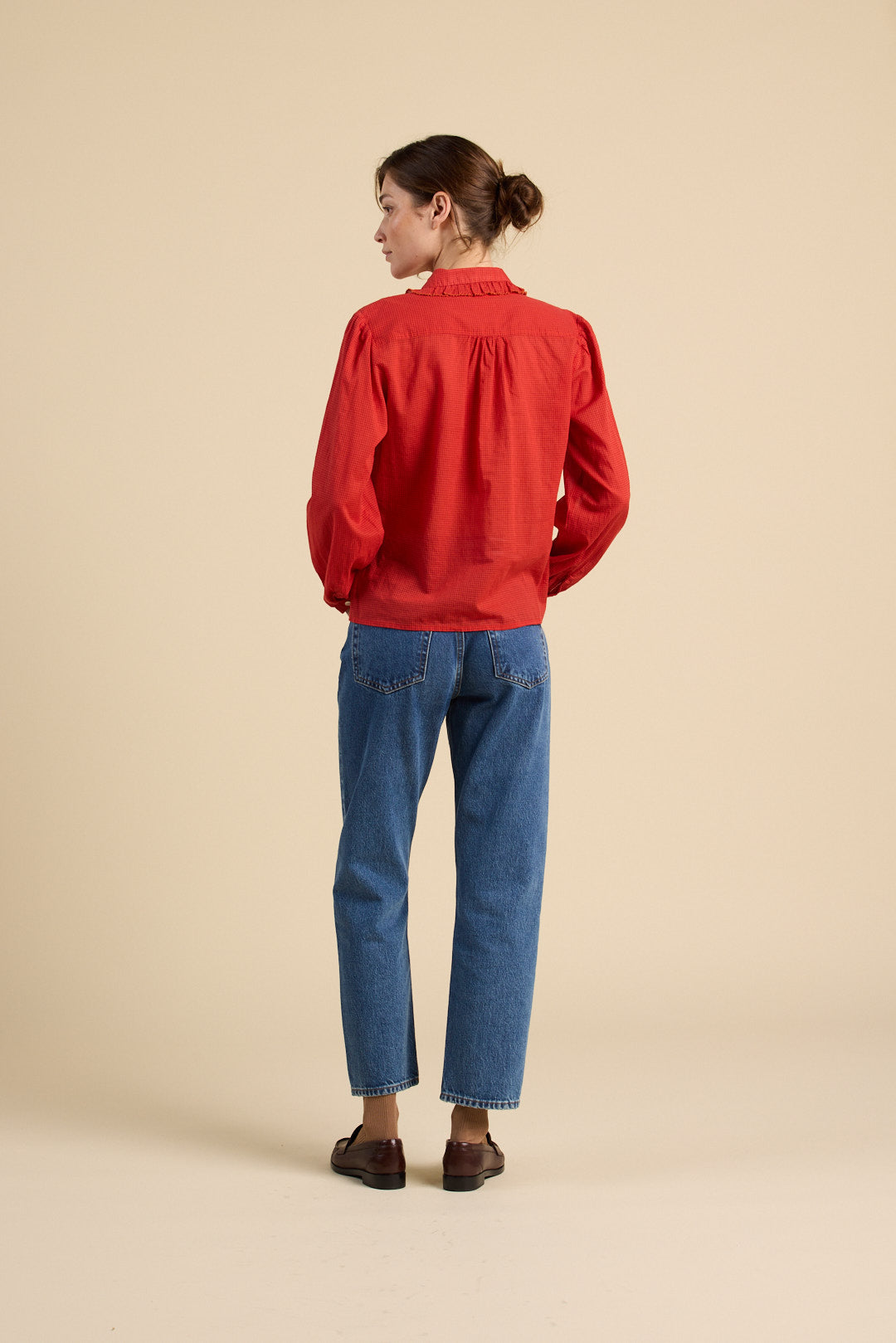 Person wearing a red shirt and blue jeans on a beige background