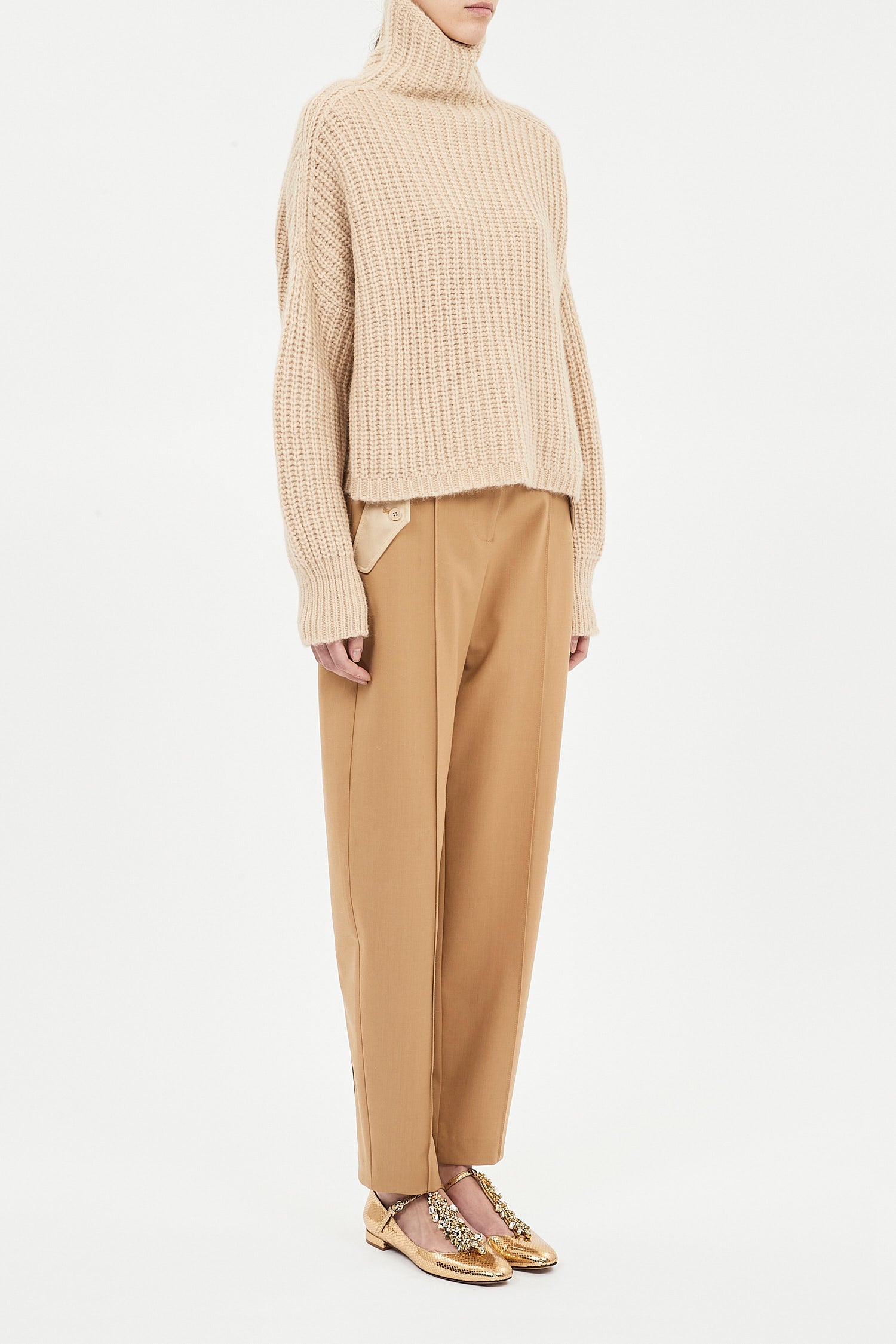 Person wearing a beige ribbed sweater and tan pants on a white background
