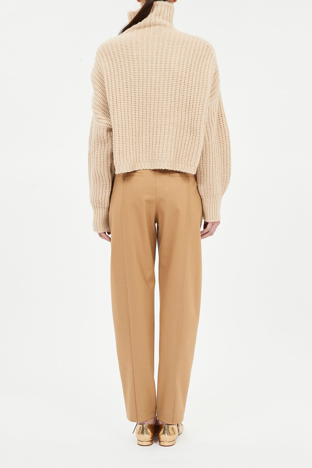 Person wearing a beige knit sweater and tan pants on a white background