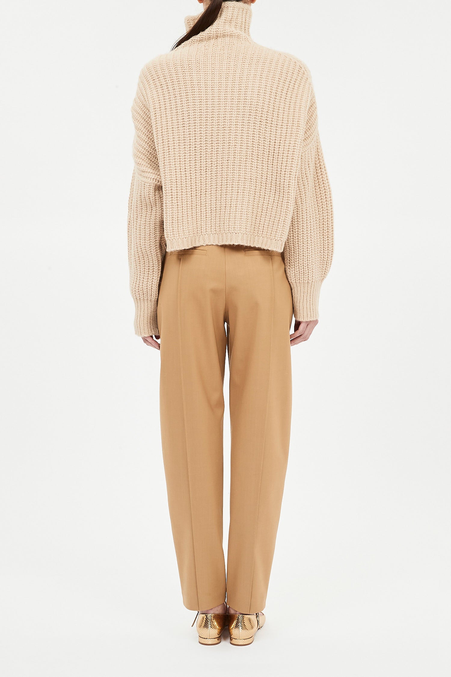 Person wearing a beige knit sweater and tan pants on a white background