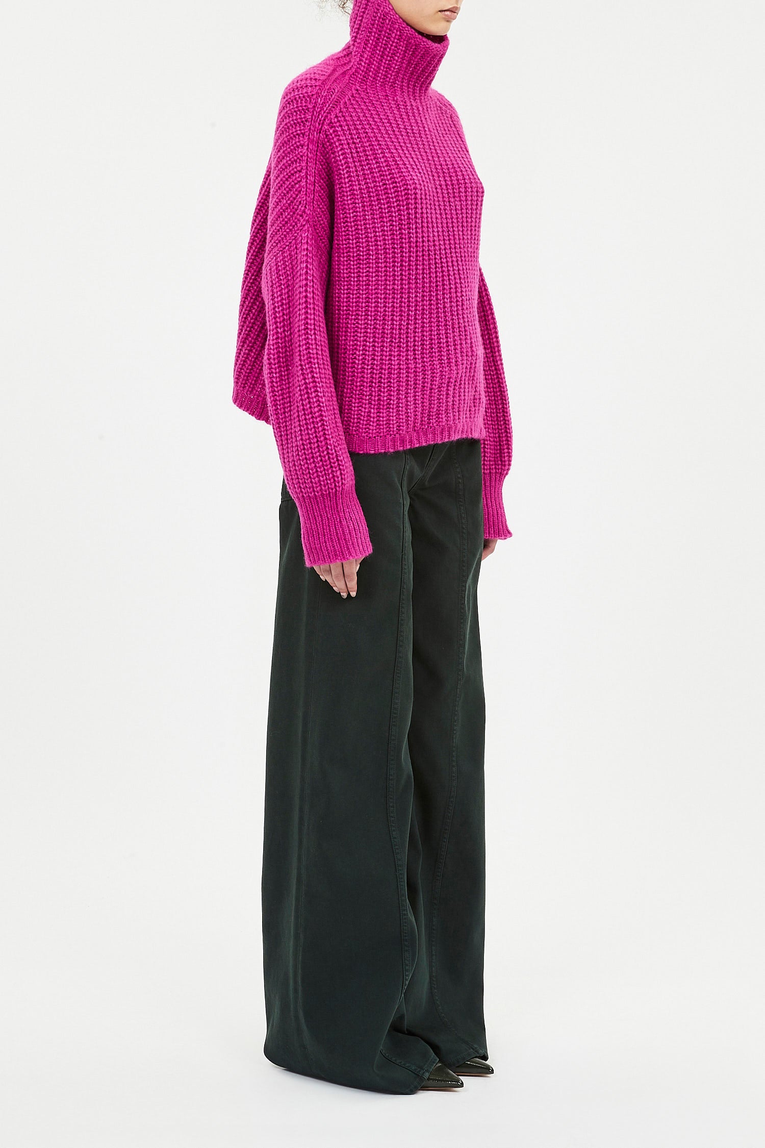 Person wearing a bright pink sweater and dark green pants on a white background