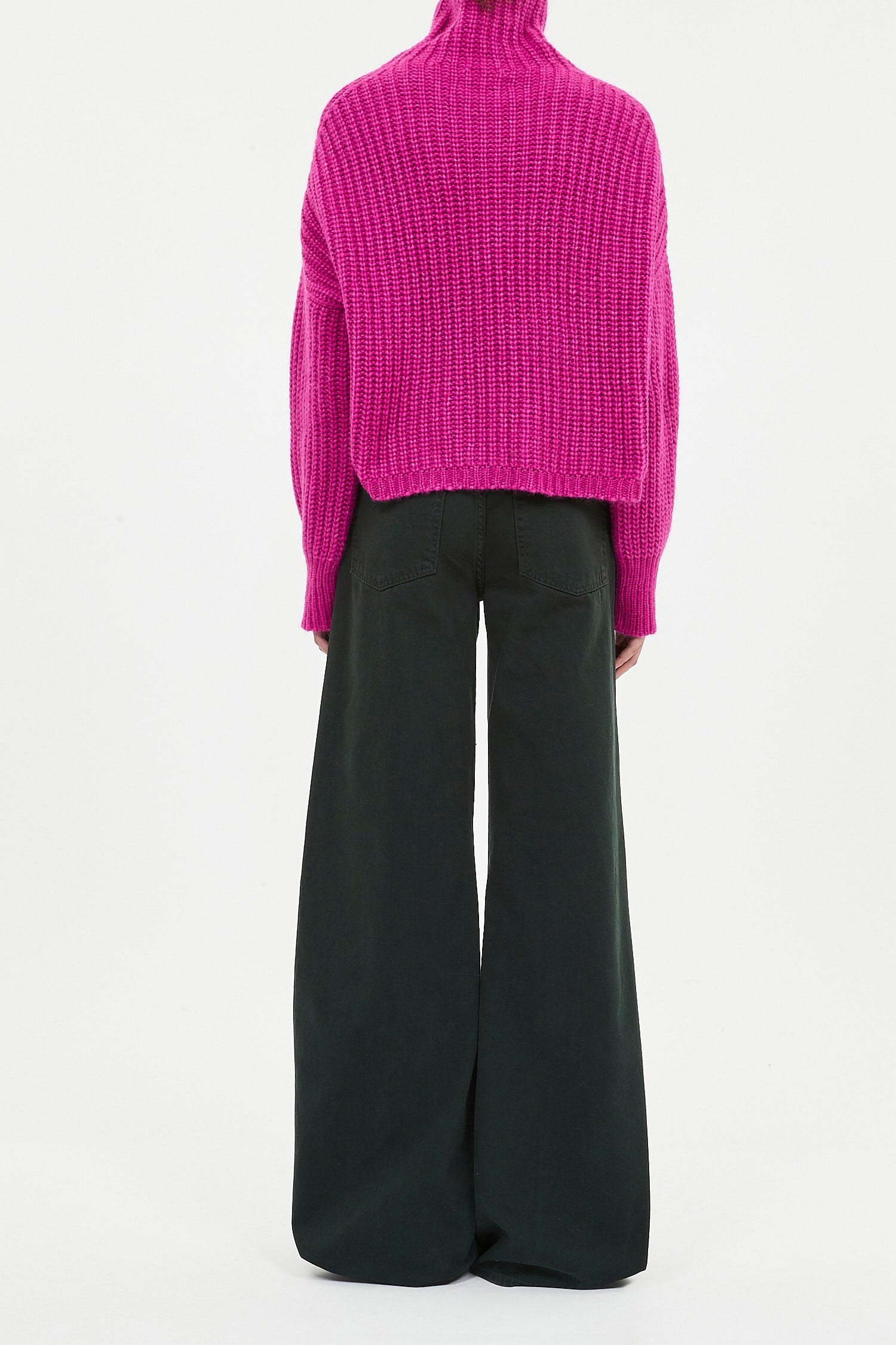 Person wearing a bright pink sweater and black pants on a white background