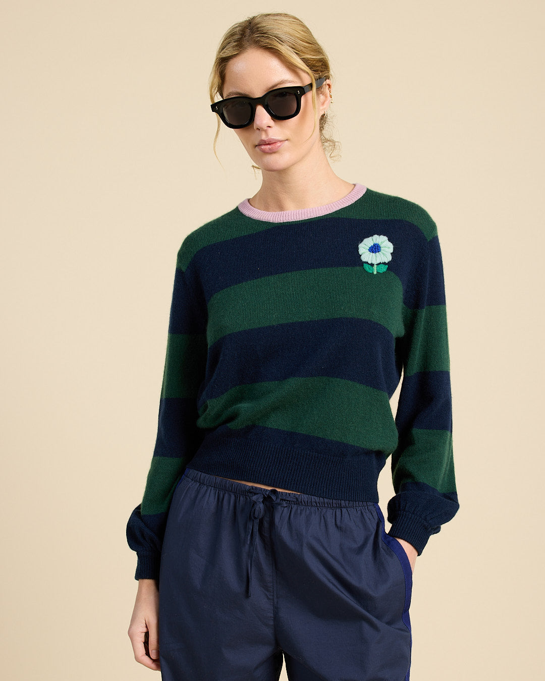 Woman wearing a green and navy striped sweater with a flower design on a beige background