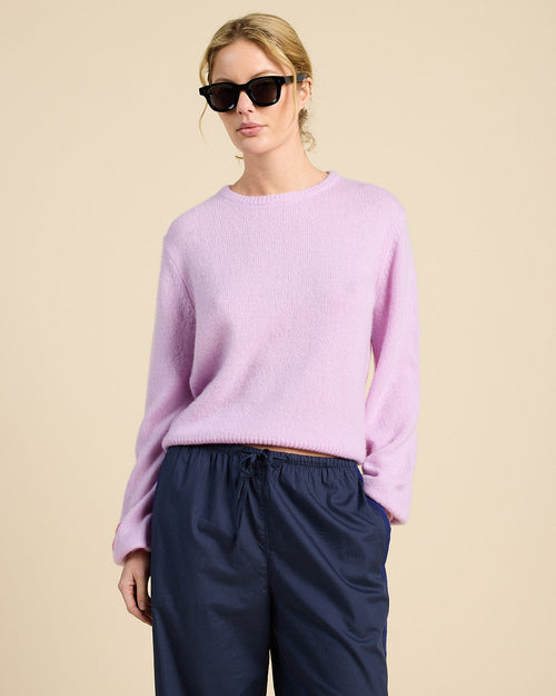 Woman wearing a light purple sweater and dark blue pants against a beige background