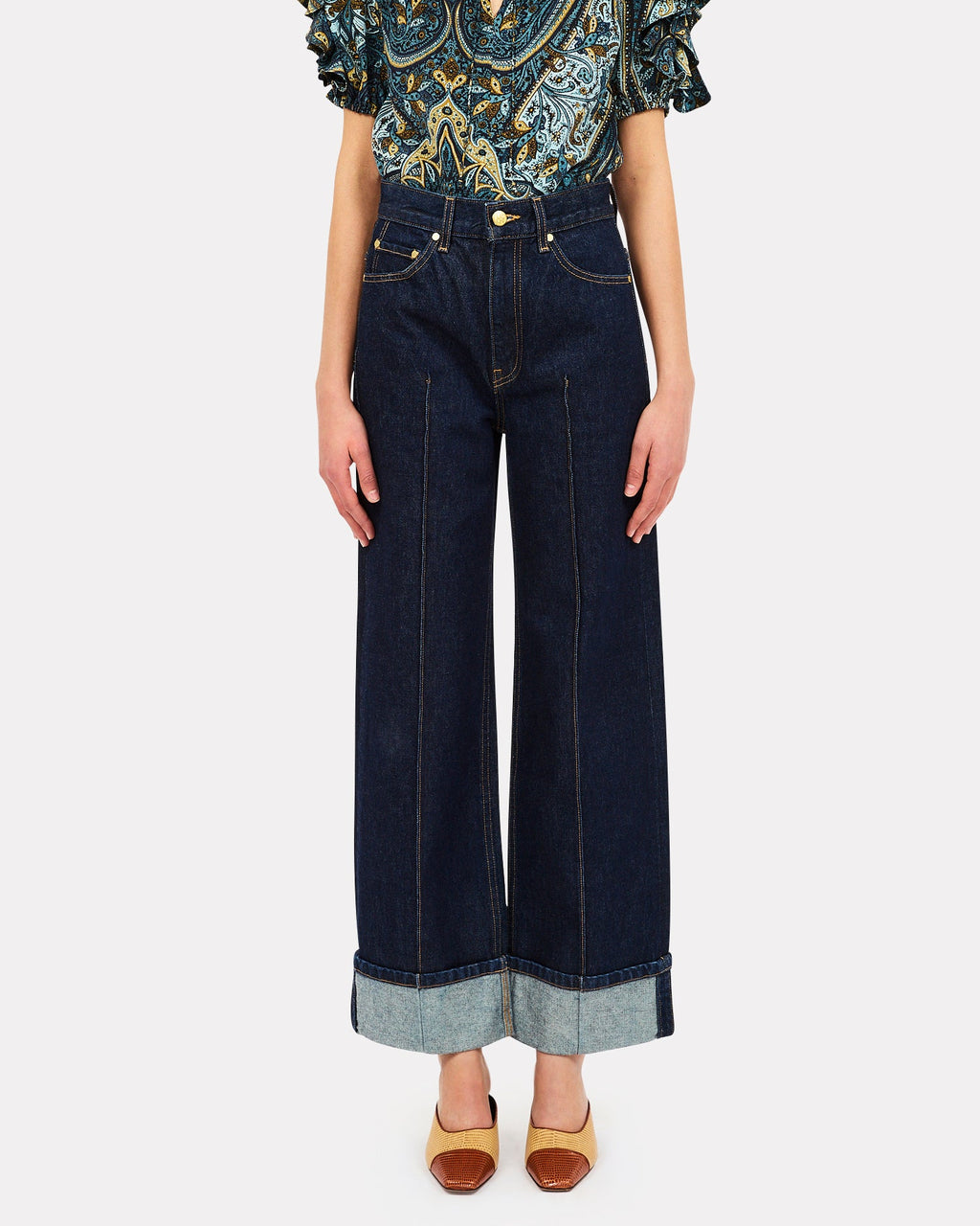 Woman wearing a patterned top and dark blue jeans on a white background