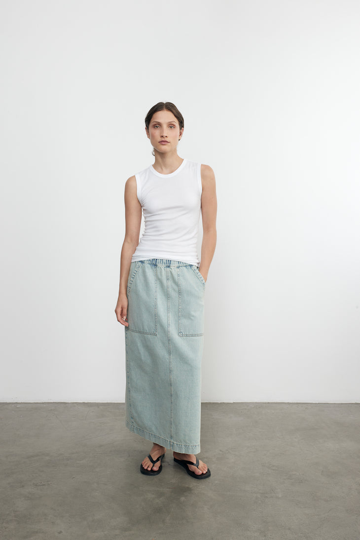 Woman wearing a white sleeveless top and light blue denim skirt against a plain white background.