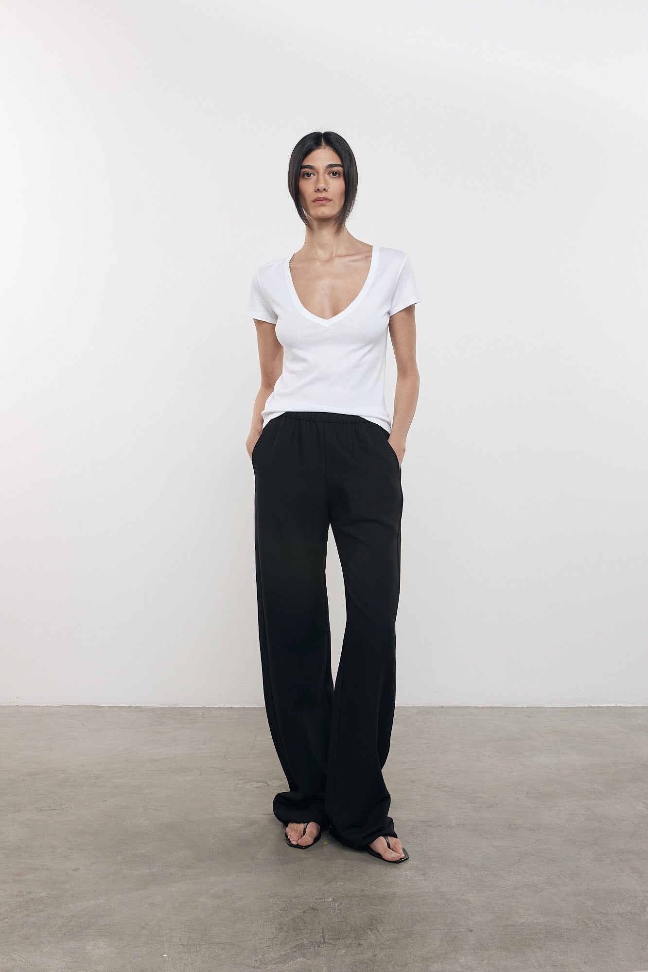 Person wearing a white top and black pants against a plain background