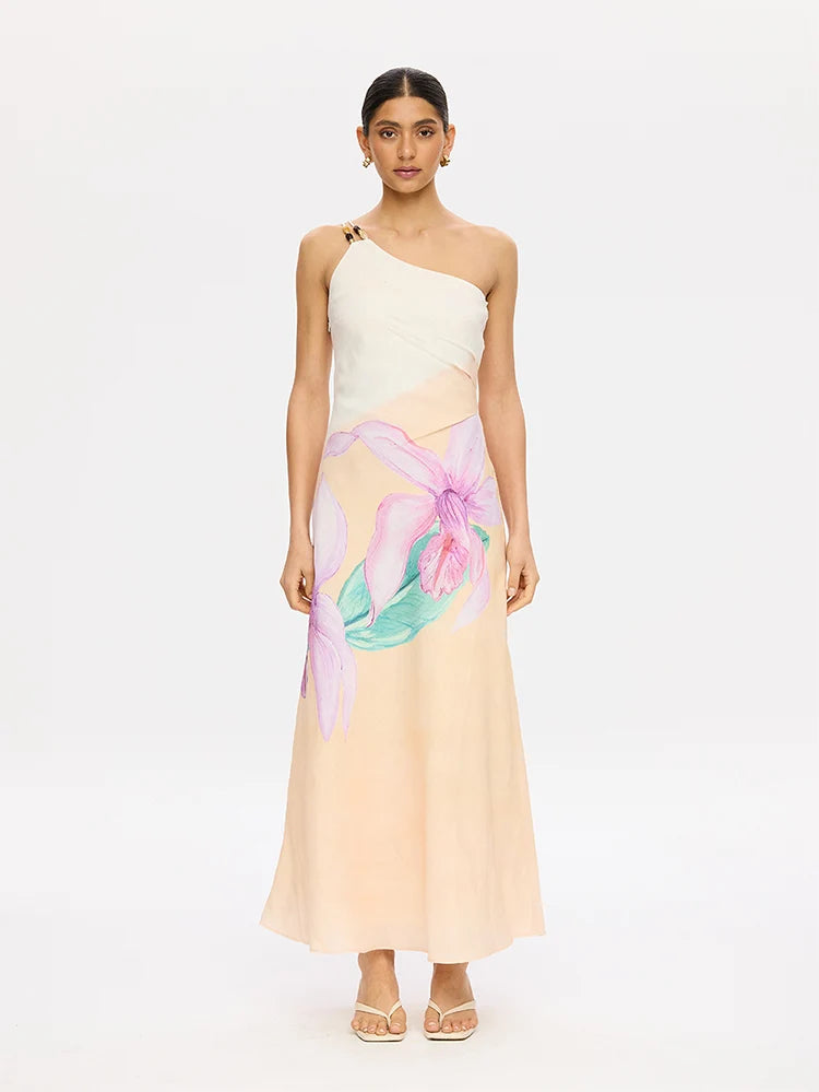 A woman modeling a one-shoulder maxi dress with a cream upper bodice, a peach lower bodice, and a large pink and teal floral print on the skirt, set against a plain white studio background.