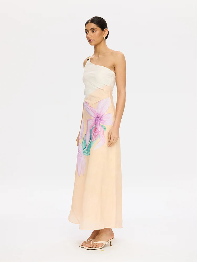 A model wearing a one-shoulder maxi dress with a white structured bodice and a flowing peach skirt featuring a large purple and teal floral print, set against a plain white studio background.