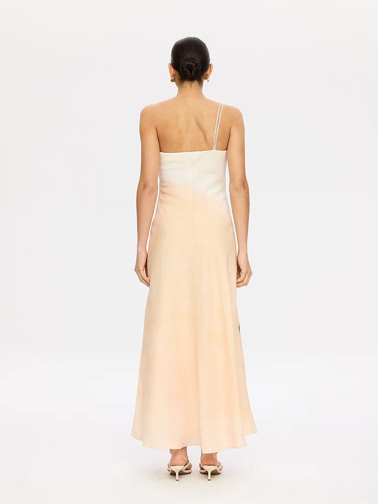 A woman viewed from the back wearing a sleeveless maxi dress with a color-blocked design, featuring a cream upper section and a pale peach lower section, on a white studio background.