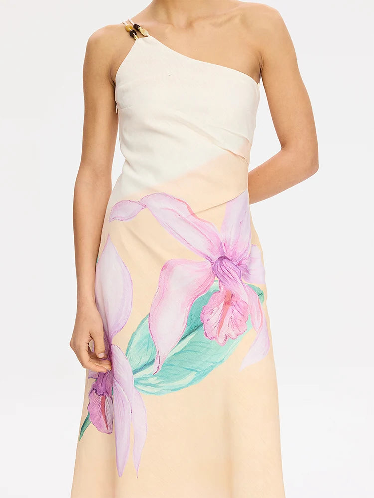 A model wearing a one-shoulder midi dress with a cream bodice and a flowing beige skirt featuring a large pink and purple orchid floral print with green leaves.