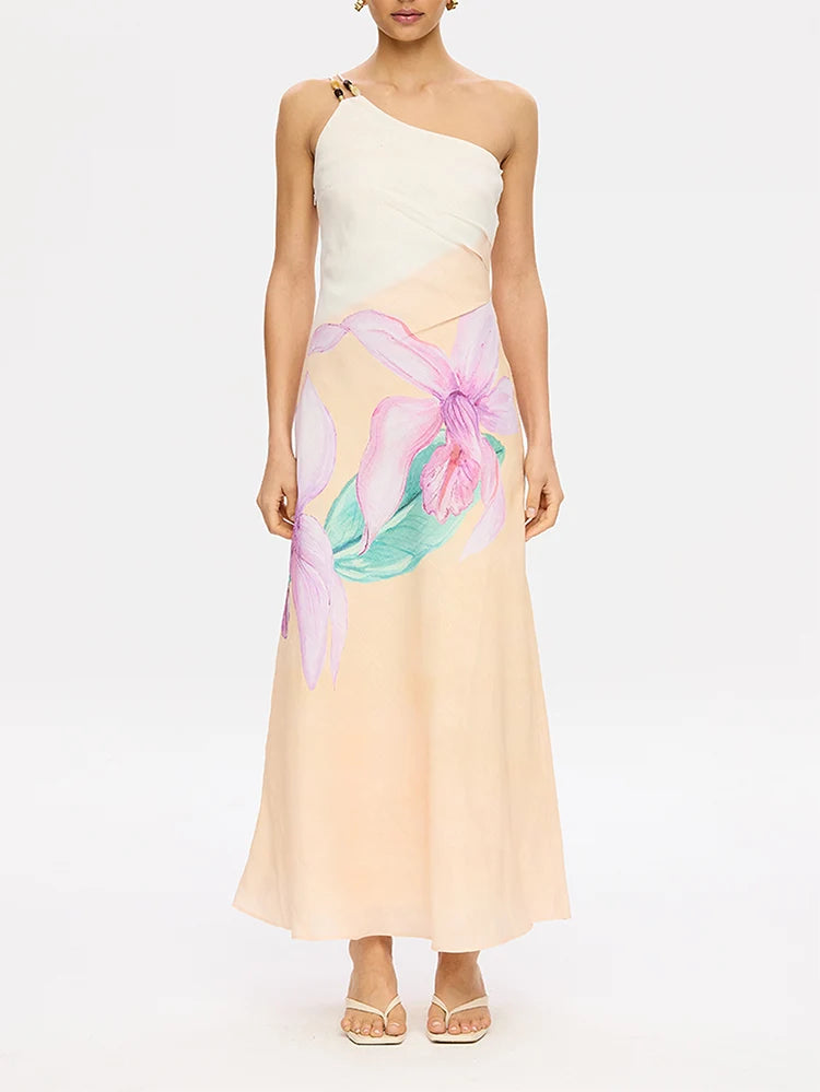 A model wearing a one-shoulder maxi dress with a cream draped bodice and a flowing peach skirt featuring a large pink and green floral print, set against a plain white studio background.