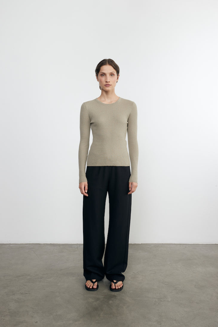 Person wearing a beige ribbed sweater and black pants on a white background