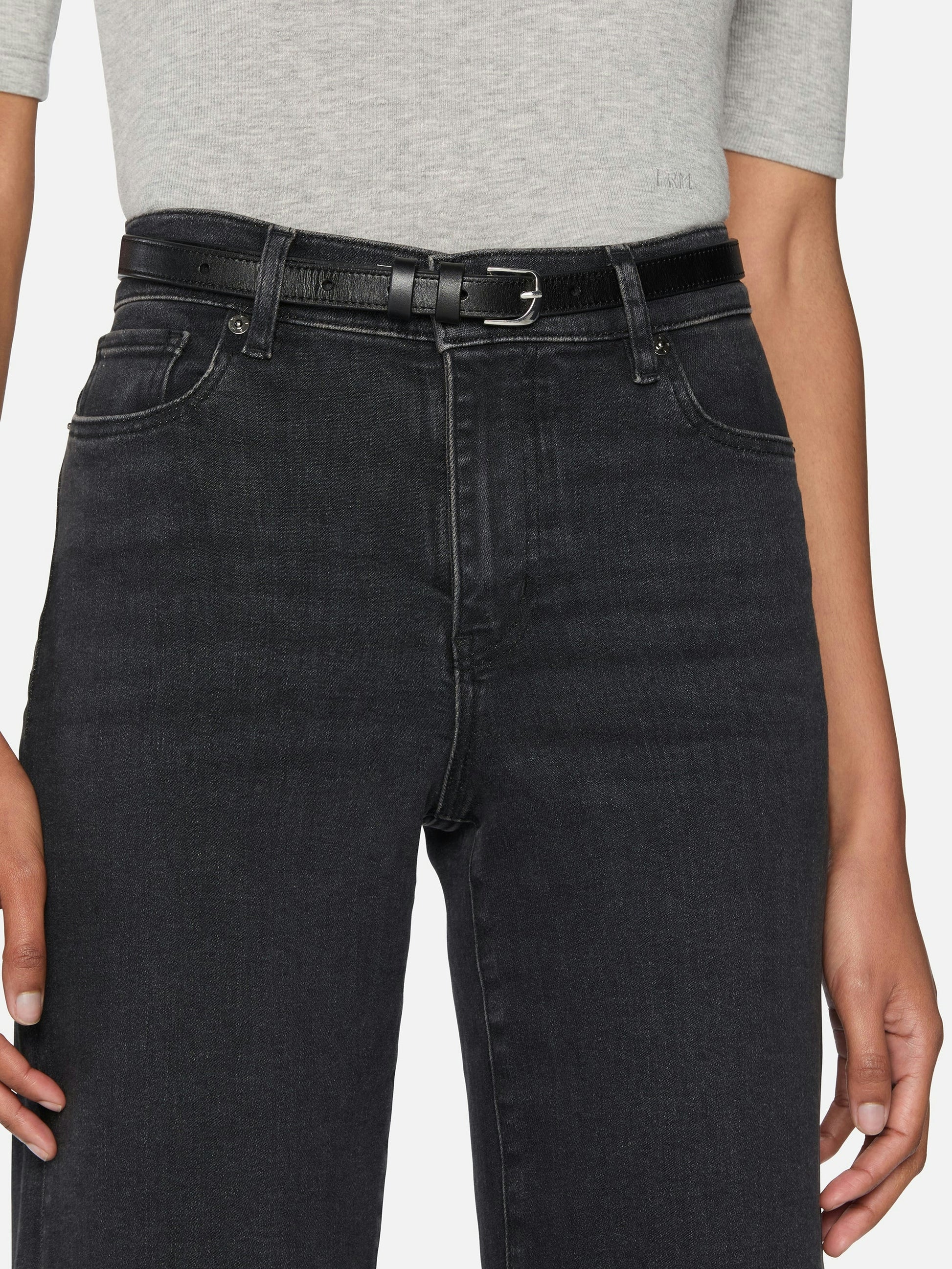 Person wearing black jeans with a belt on a plain background