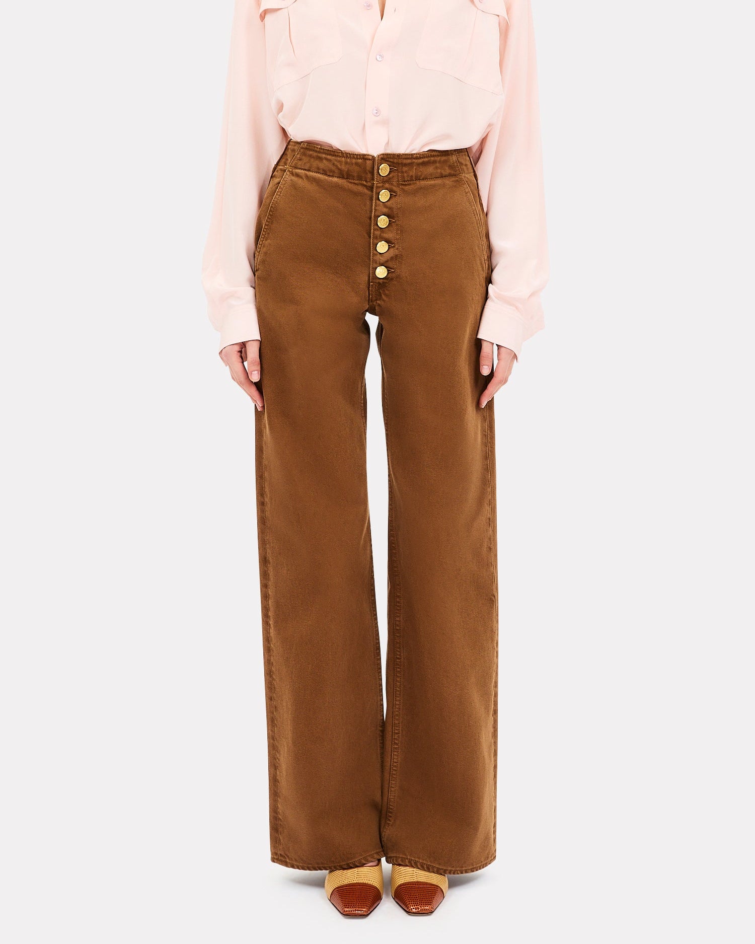 Person wearing a light pink blouse and brown high-waisted pants on a white background
