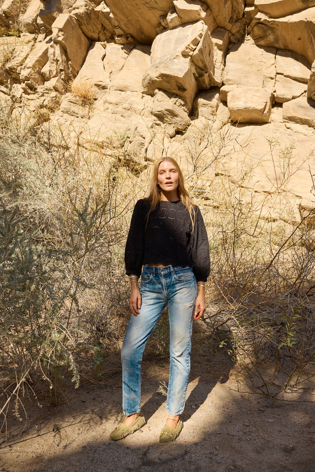 Person standing in a desert landscape with rocky formations and sparse vegetation.