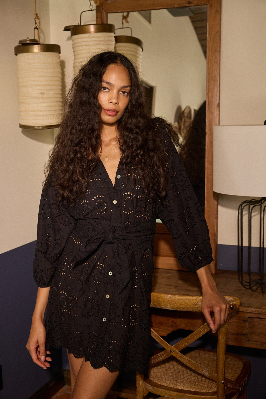 Woman in a black dress standing in a room with wooden furniture and hanging lights.