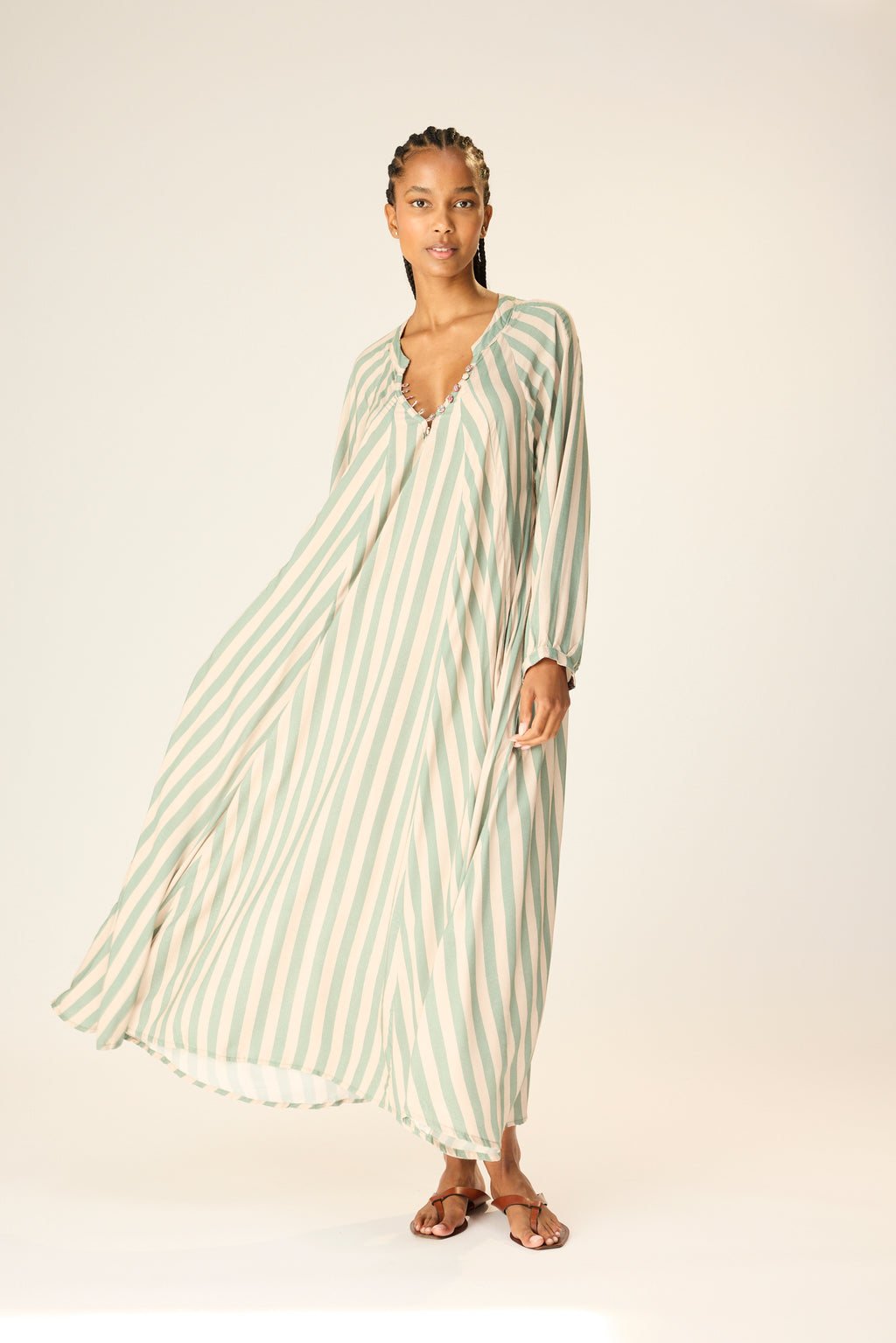 Woman wearing a long, light-colored striped dress on a plain background