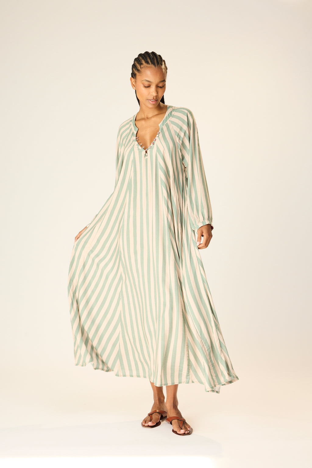 Woman wearing a long, light-colored striped dress on a plain background