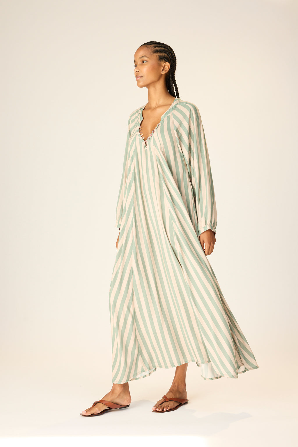 Woman wearing a long, light green and white striped dress on a plain background