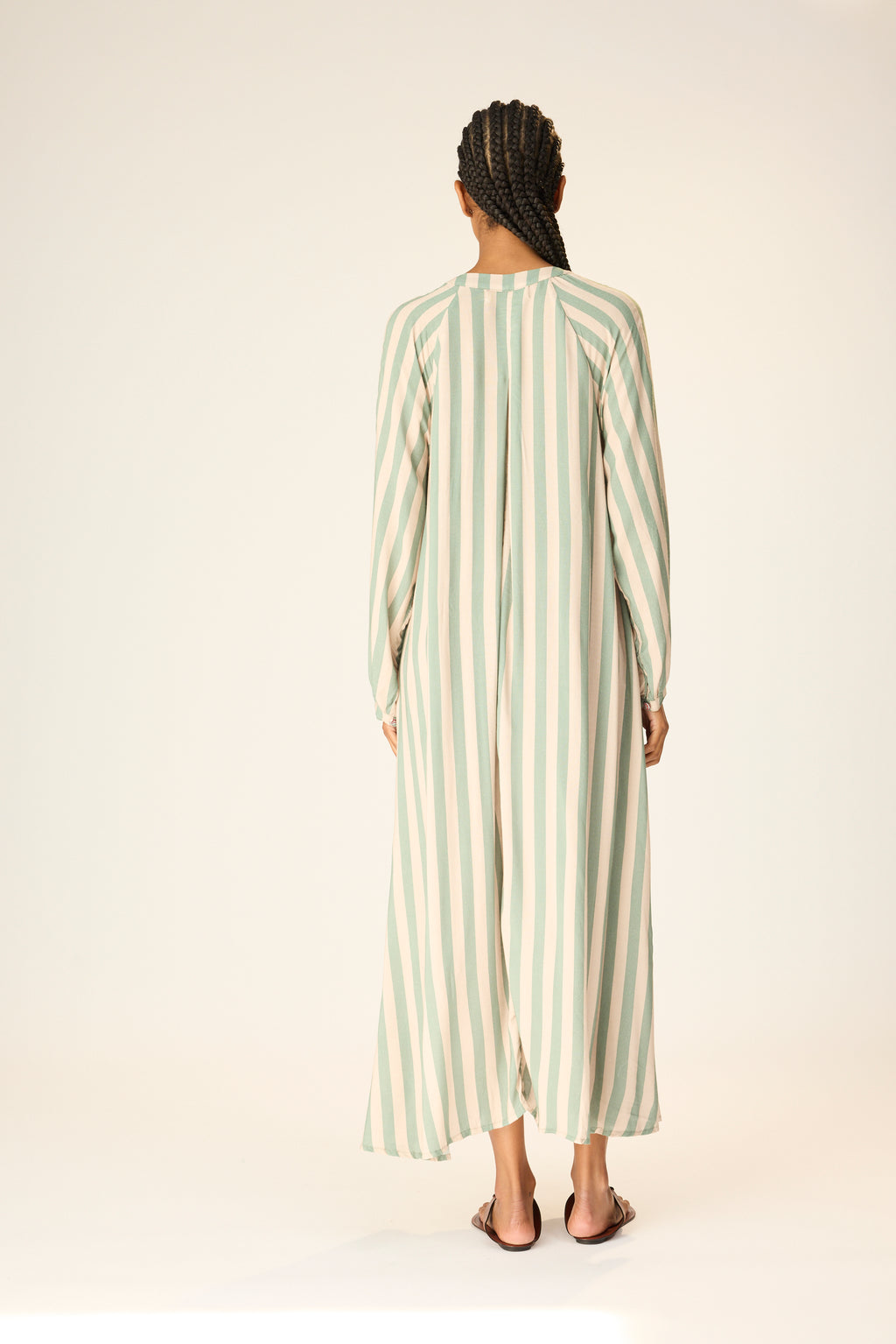 Woman wearing a long, light green and white striped dress on a plain background