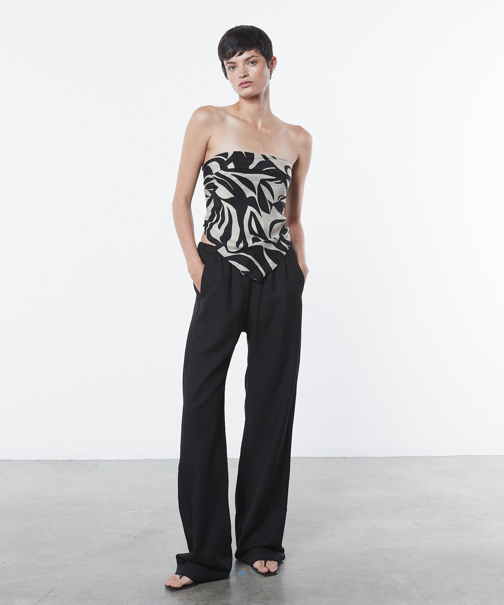 Woman wearing a strapless top with a black and white pattern and black pants on a white background