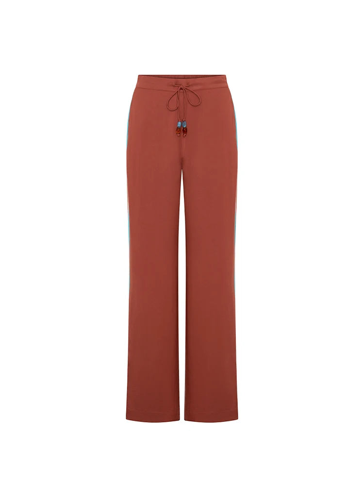 A pair of wide-leg trousers in a terracotta rust color, featuring a drawstring waist and thin light blue side stripes, shown against a plain white background.