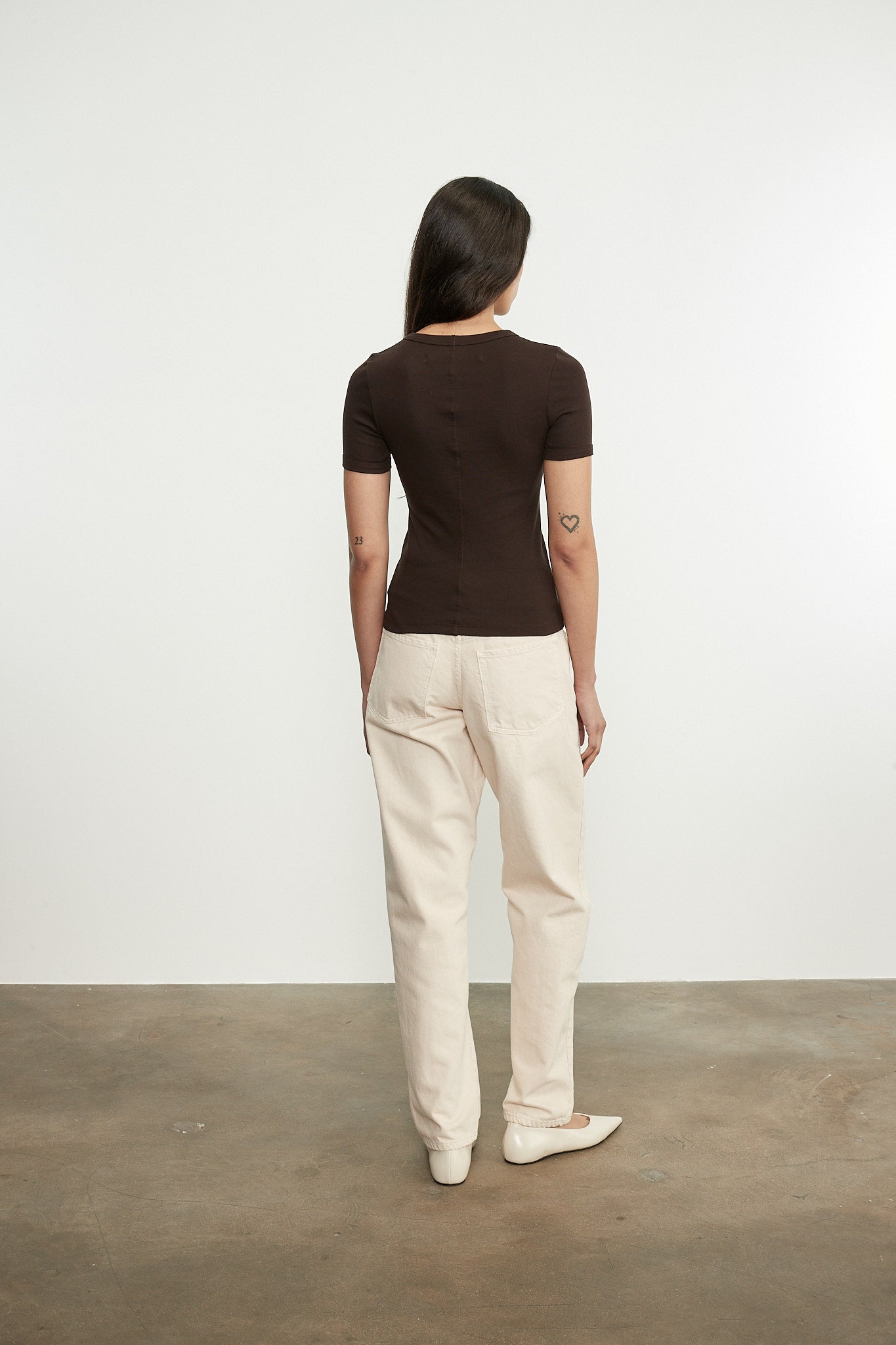 Person wearing a brown top and beige pants standing against a white wall.
